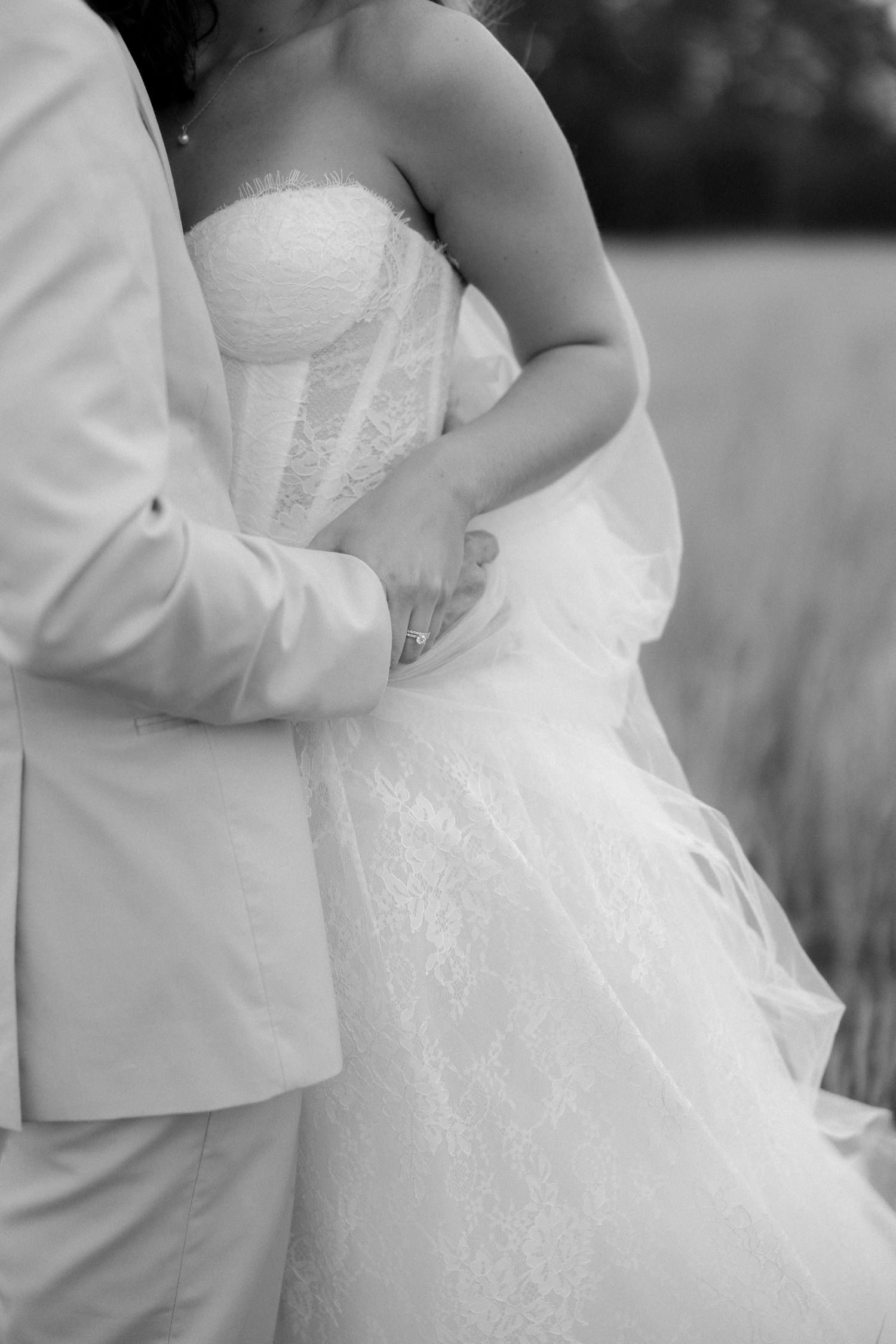 Black and white close-up of groom holding bride's waist in lace wedding dress.