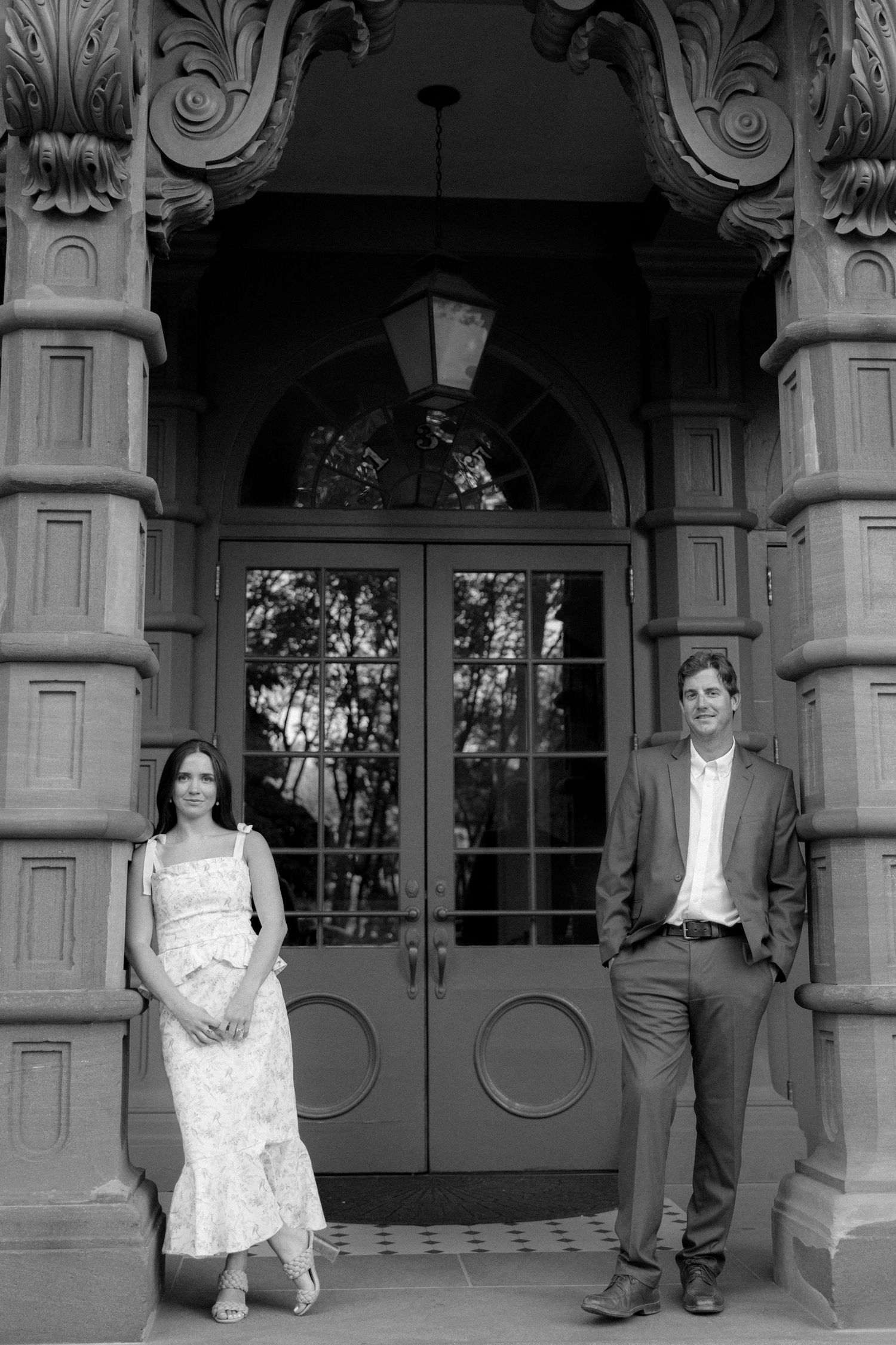 Black and white photo of a couple standing in front of an ornate building entrance with decorative columns and a lantern.