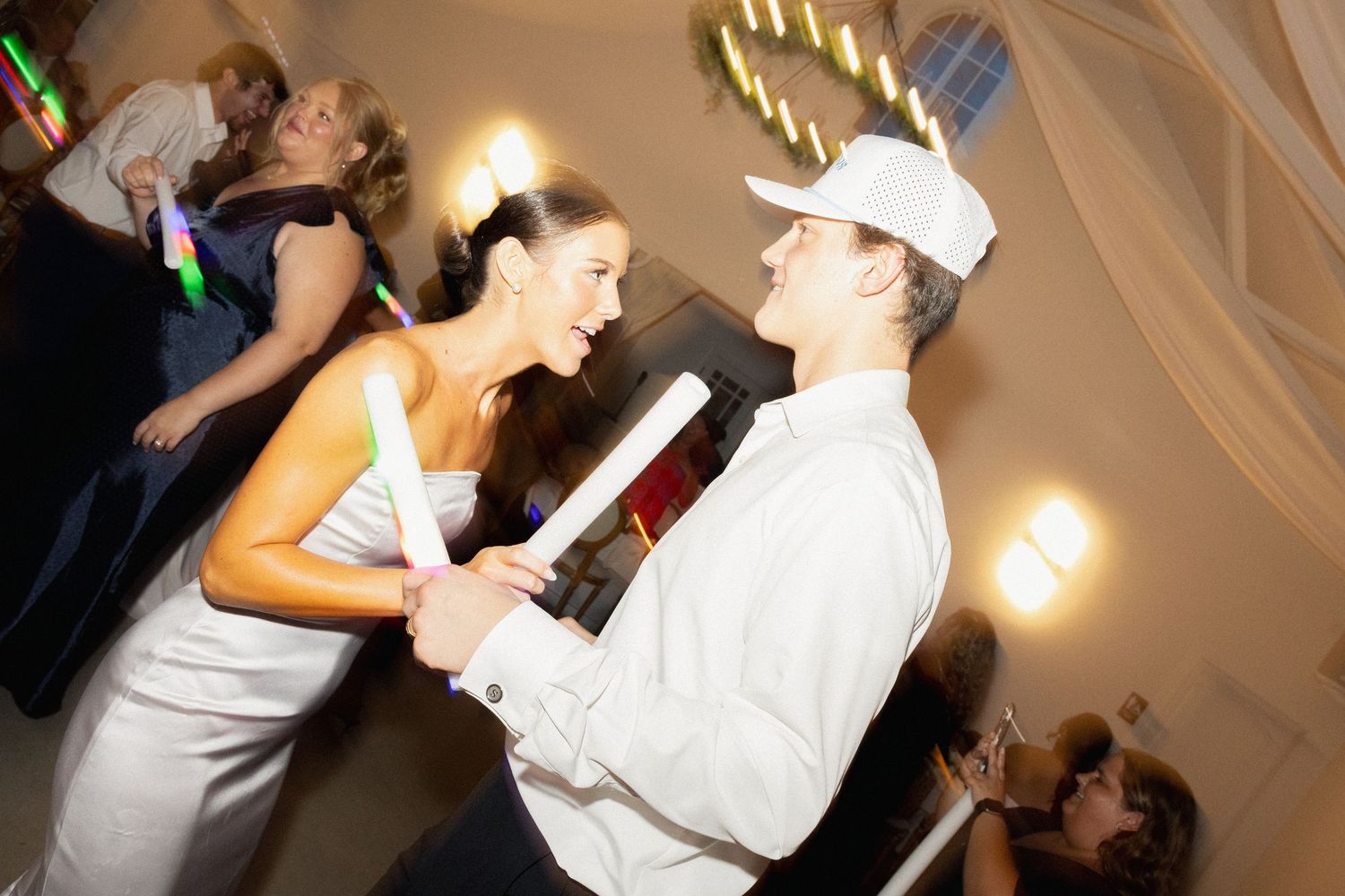 Bride and groom dancing together at a wedding reception while holding glow sticks on the dance floor.