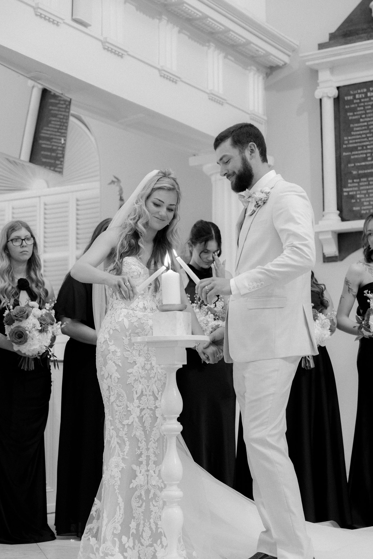 Black and white photo of bride and groom lighting a unity candle together during their church ceremony.