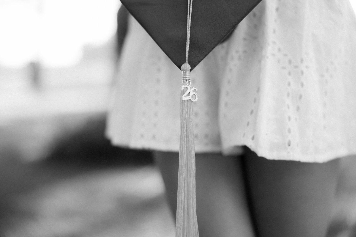 Black and white close-up of graduation cap tassel with 2026 charm against white skirt.