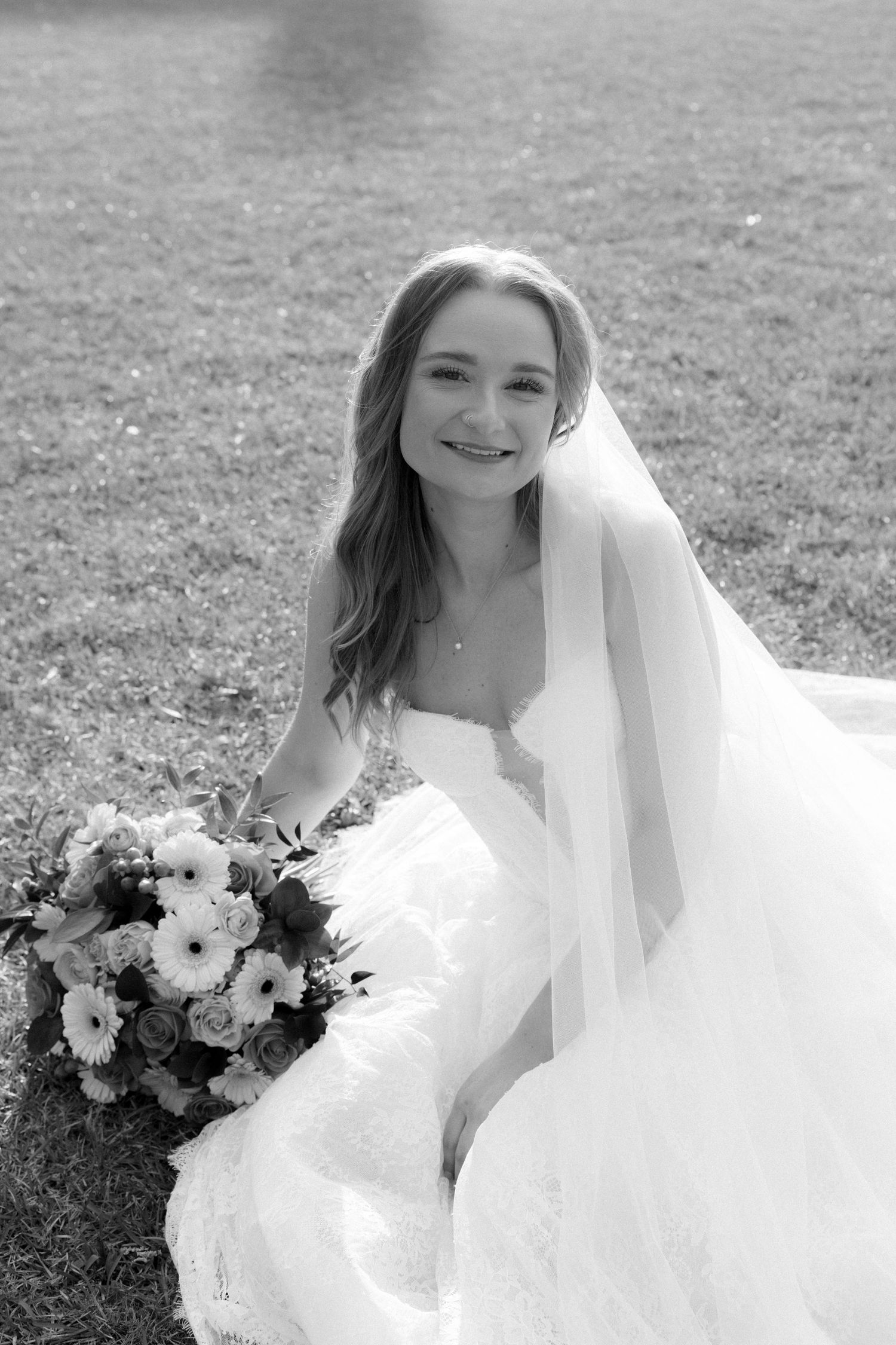 Black and white portrait of smiling bride in lace gown with bouquet.