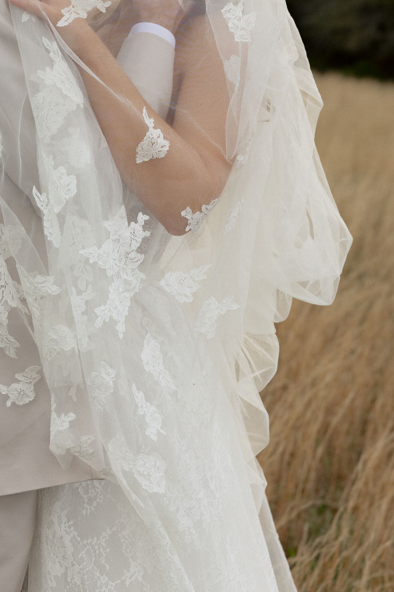 Close-up of bride in lace wedding dress with floral applique details and flowing veil.