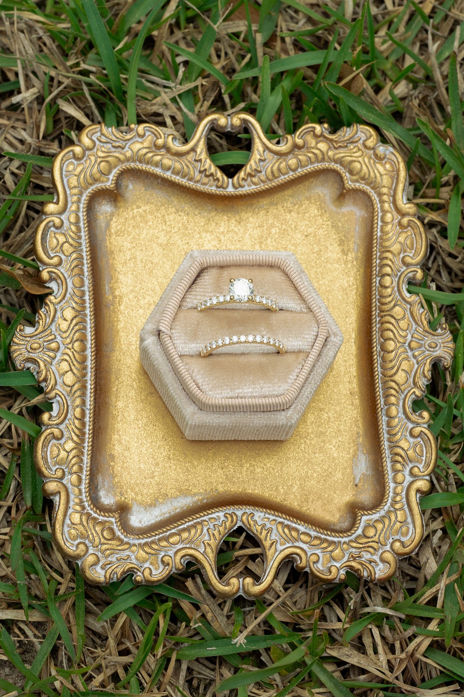 Diamond engagement ring and wedding band displayed in velvet hexagon box on ornate gold vintage tray.