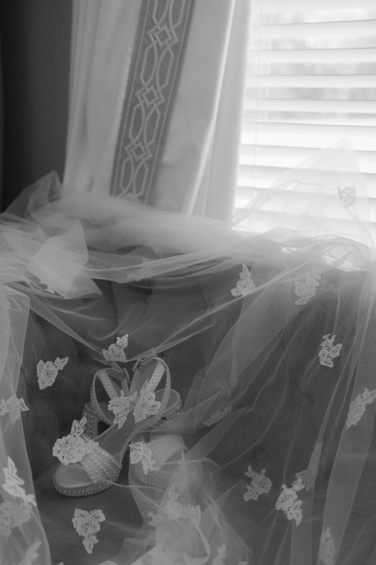 Black and white photo of lace bridal veil draped over a couch with wedding heels peeking through.