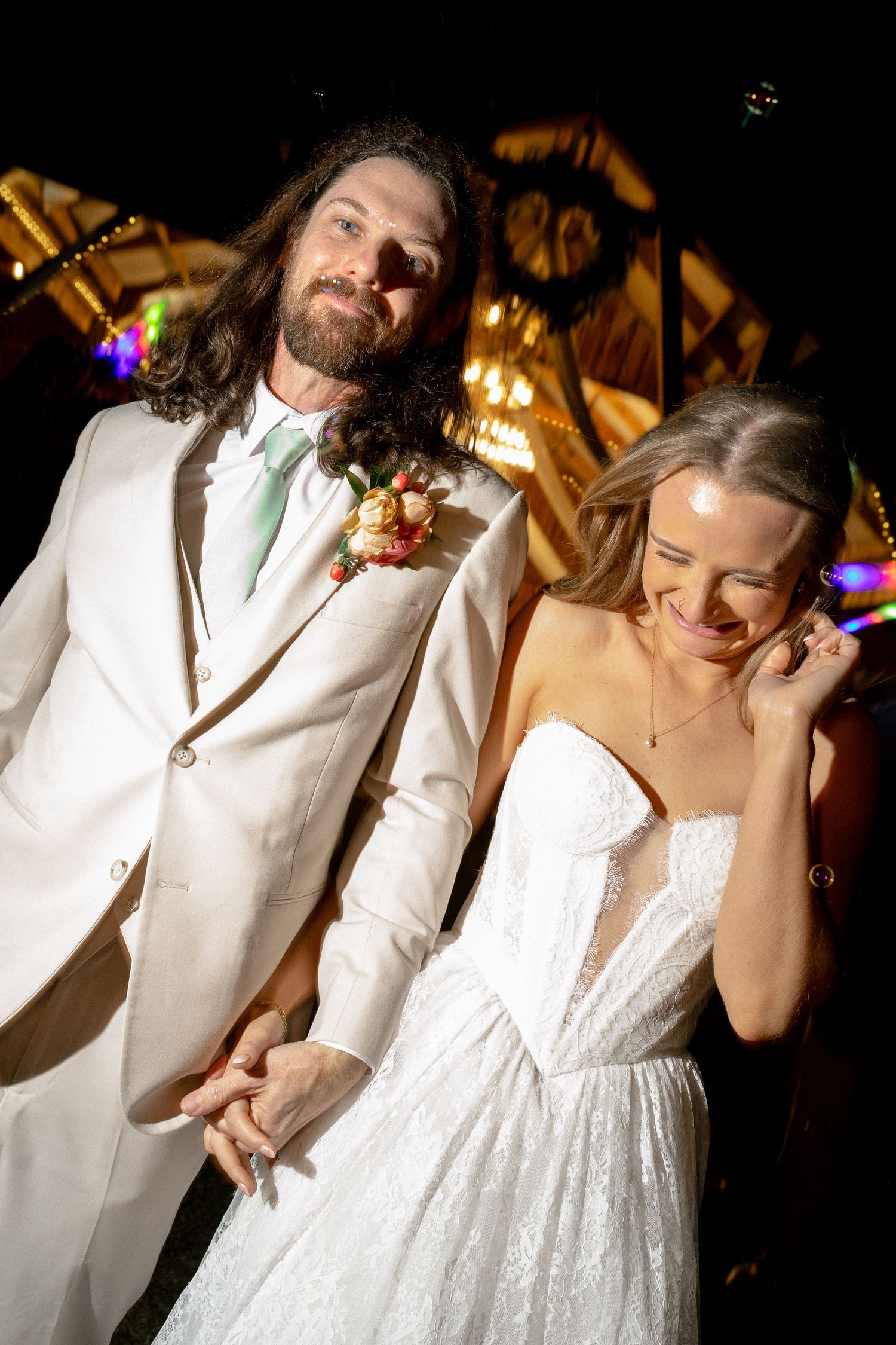 Bride laughing joyfully while holding grooms hand during wedding reception exit.