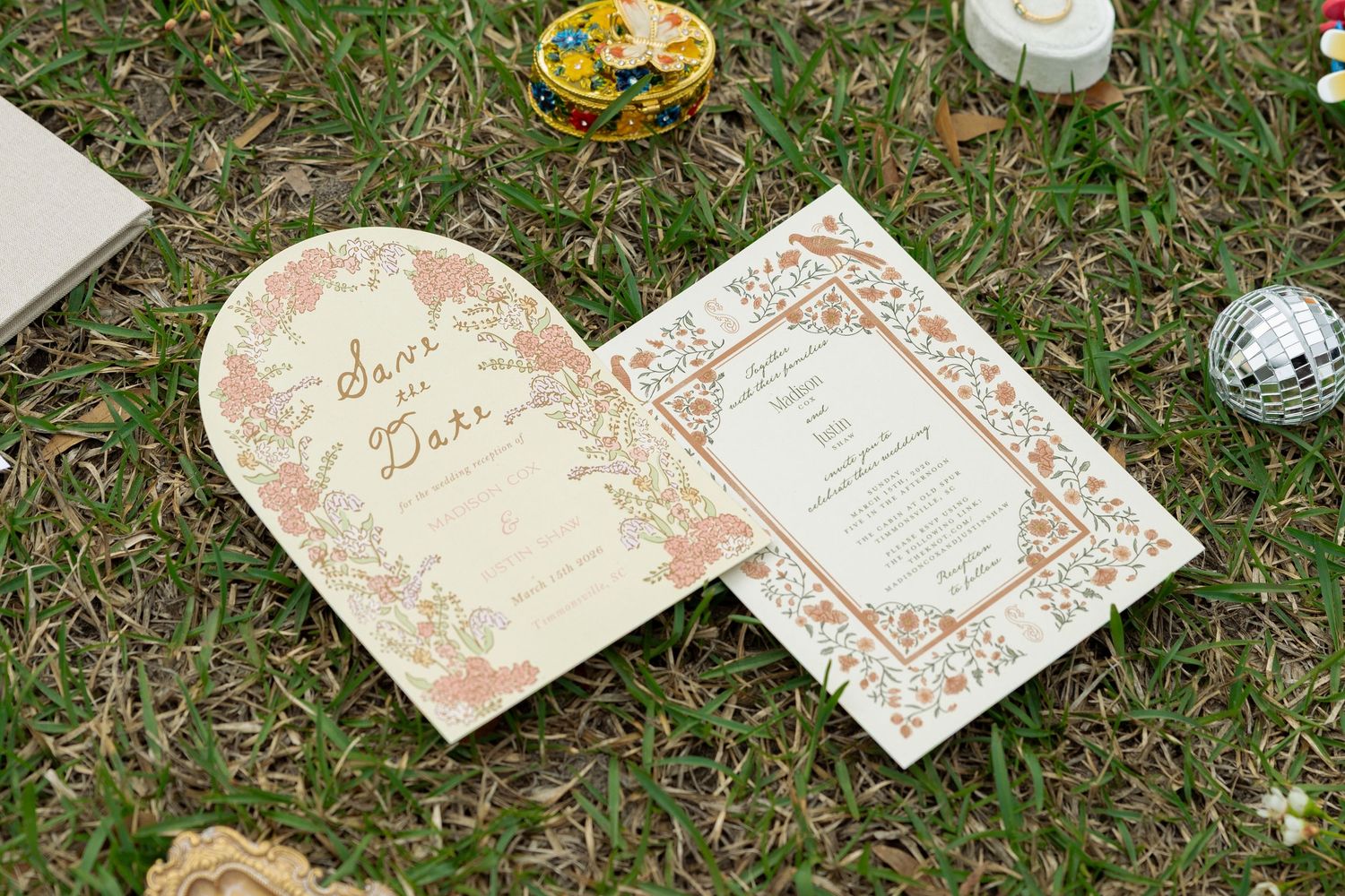 Arch-shaped floral Save the Date card and botanical wedding invitation suite displayed on green grass.