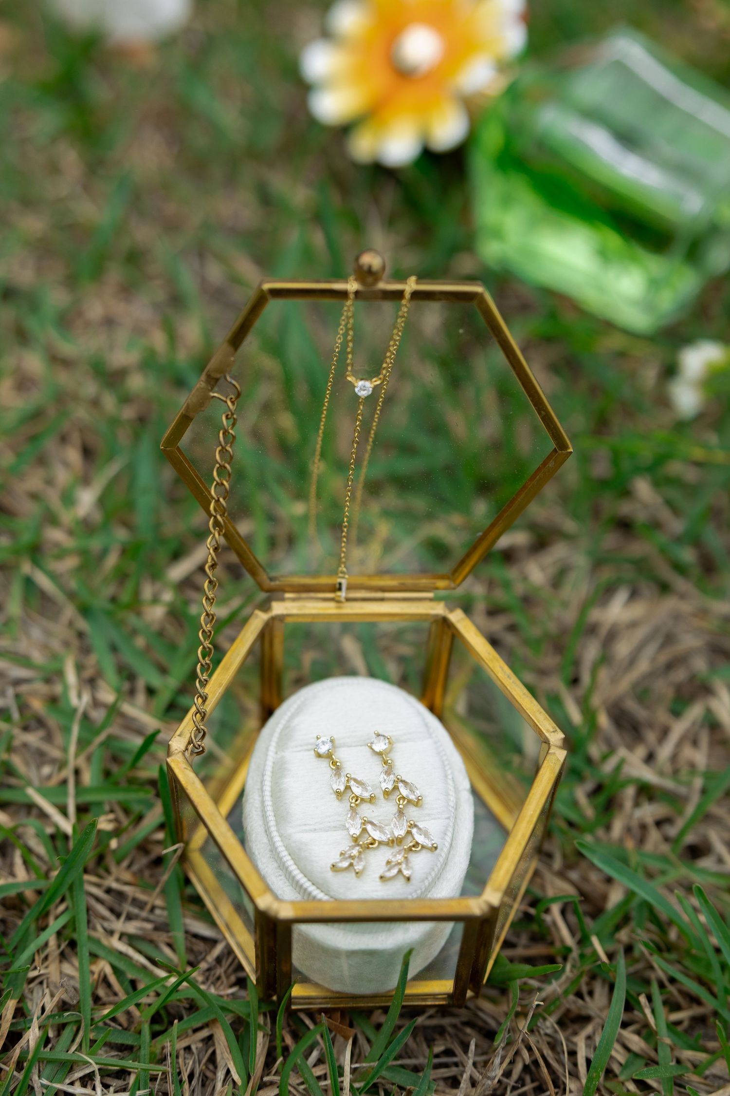 Gold hexagonal glass jewelry box containing a delicate gold necklace and earrings on a white cushion.