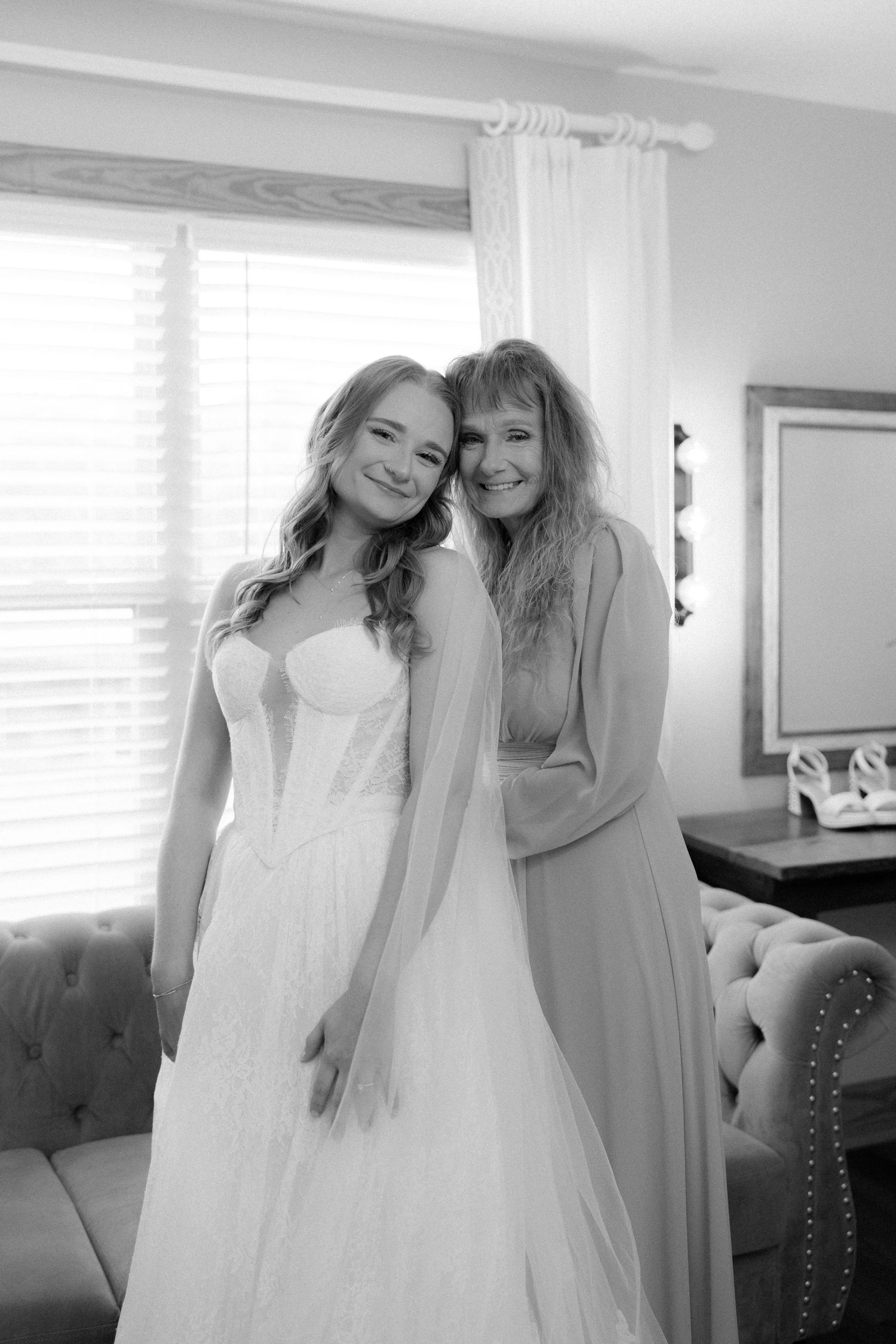 Black and white portrait of smiling bride in wedding gown with mother in getting ready room.