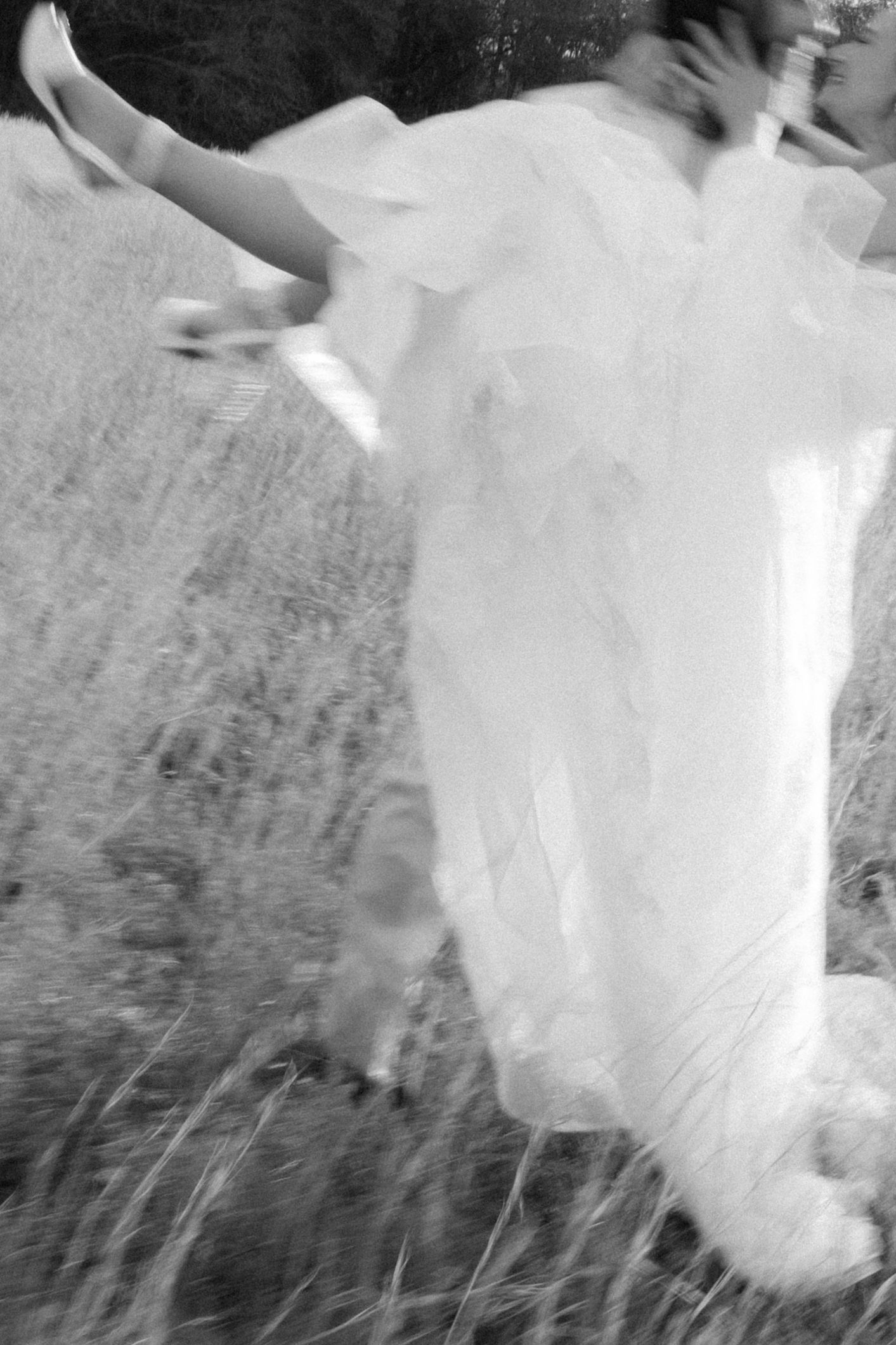 Black and white motion-blurred photo of bride in flowing gown running through a field.