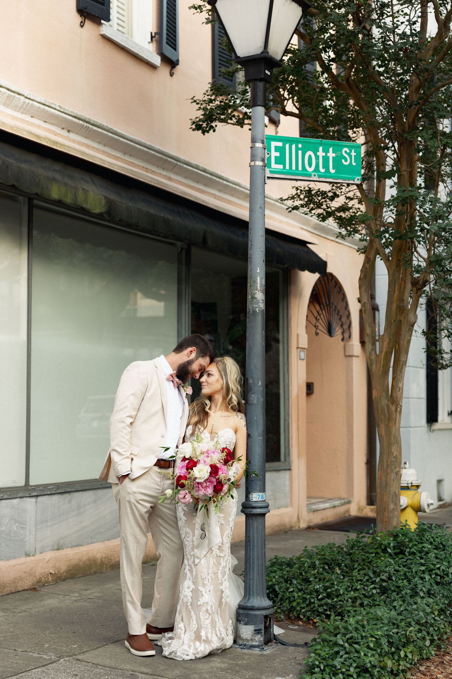 Bride and groom share a romantic moment under Elliott St sign, bride holding colorful bouquet.