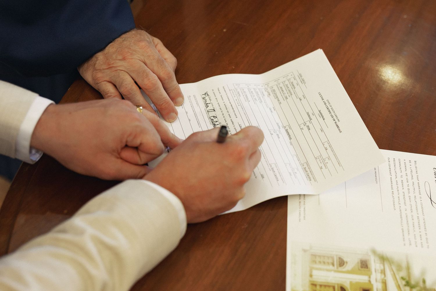 Two people signing an important document with a pen on a wooden table during a formal meeting.
