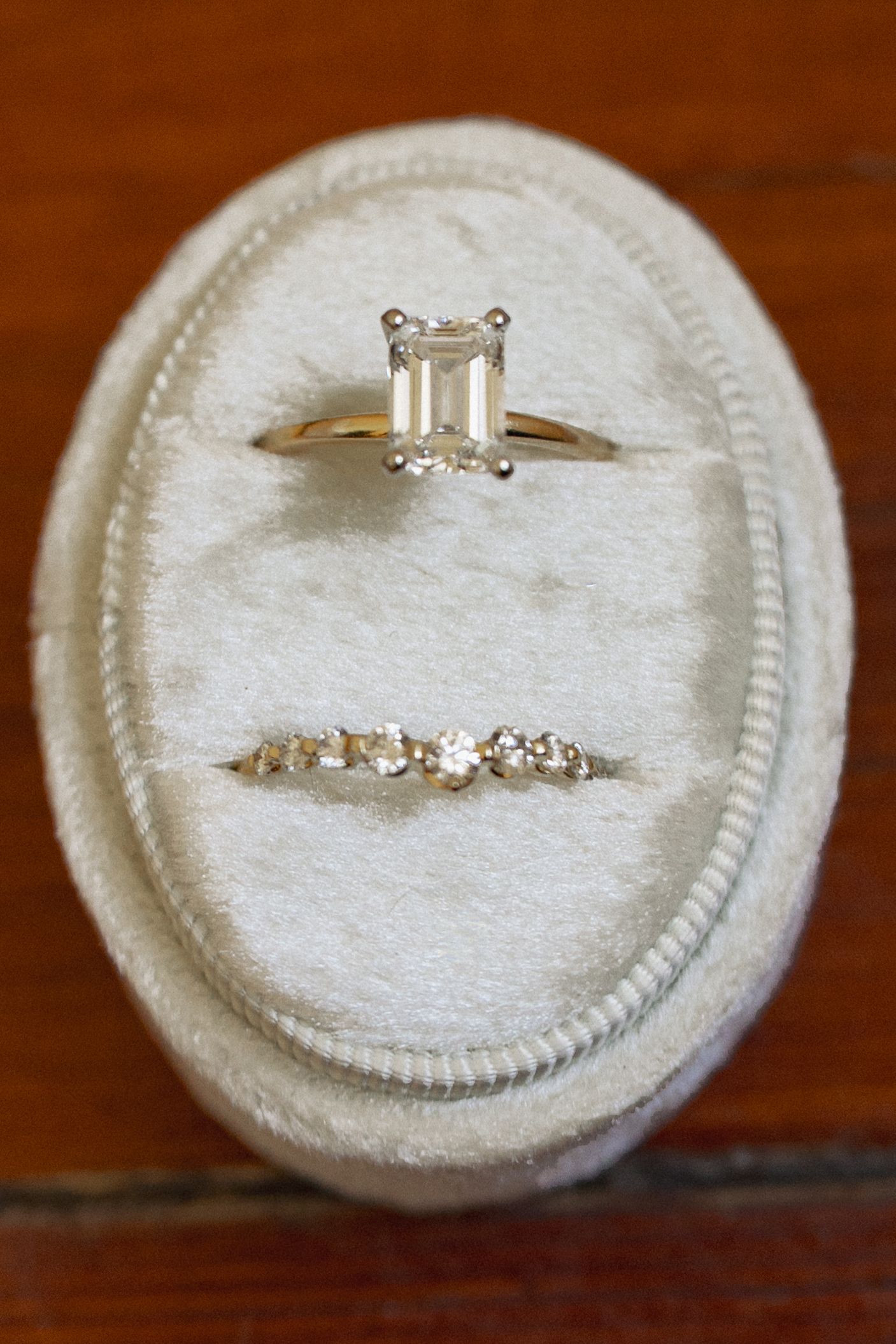 Emerald cut diamond solitaire engagement ring paired with diamond band in ivory velvet ring box.
