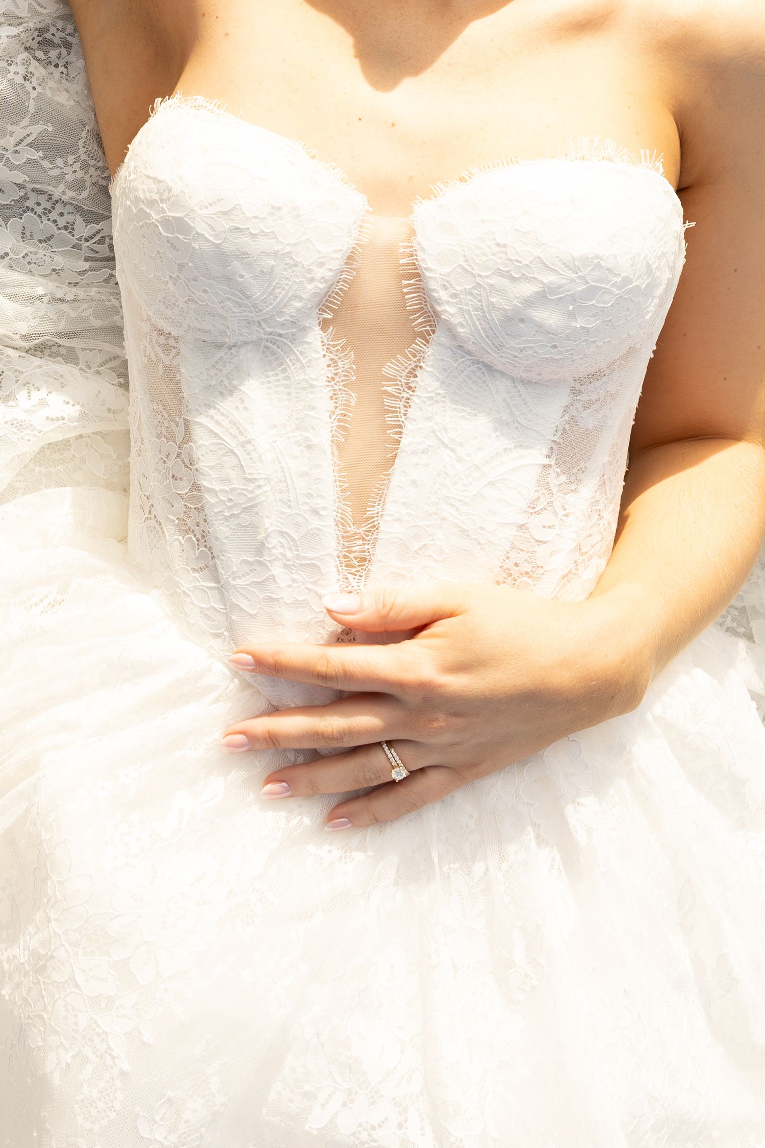 Close-up of bride in strapless lace corset wedding dress with hands folded, wearing engagement ring.