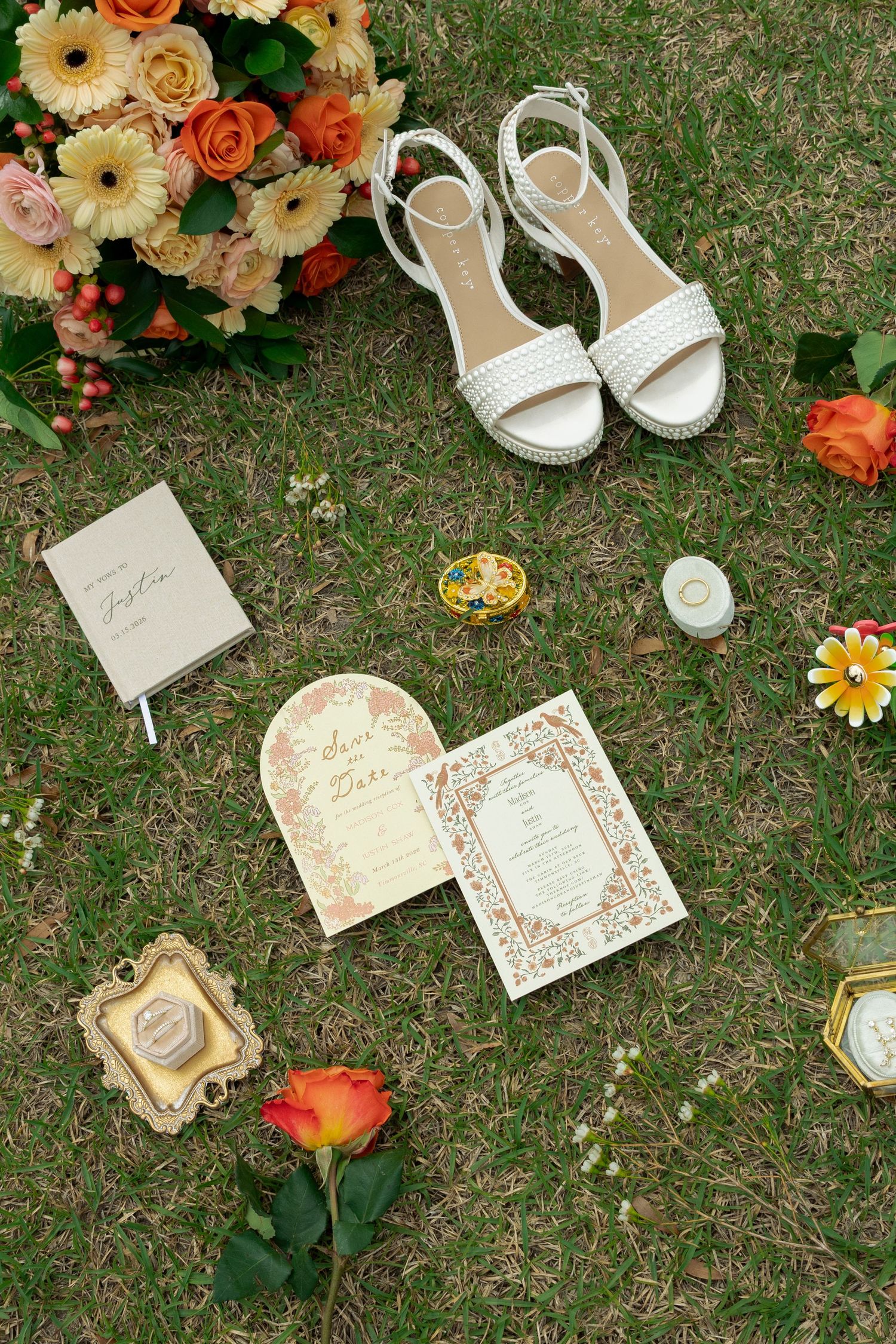 Elegant wedding flat lay with floral bouquet, white platform heels, invitations, and accessories on grass.