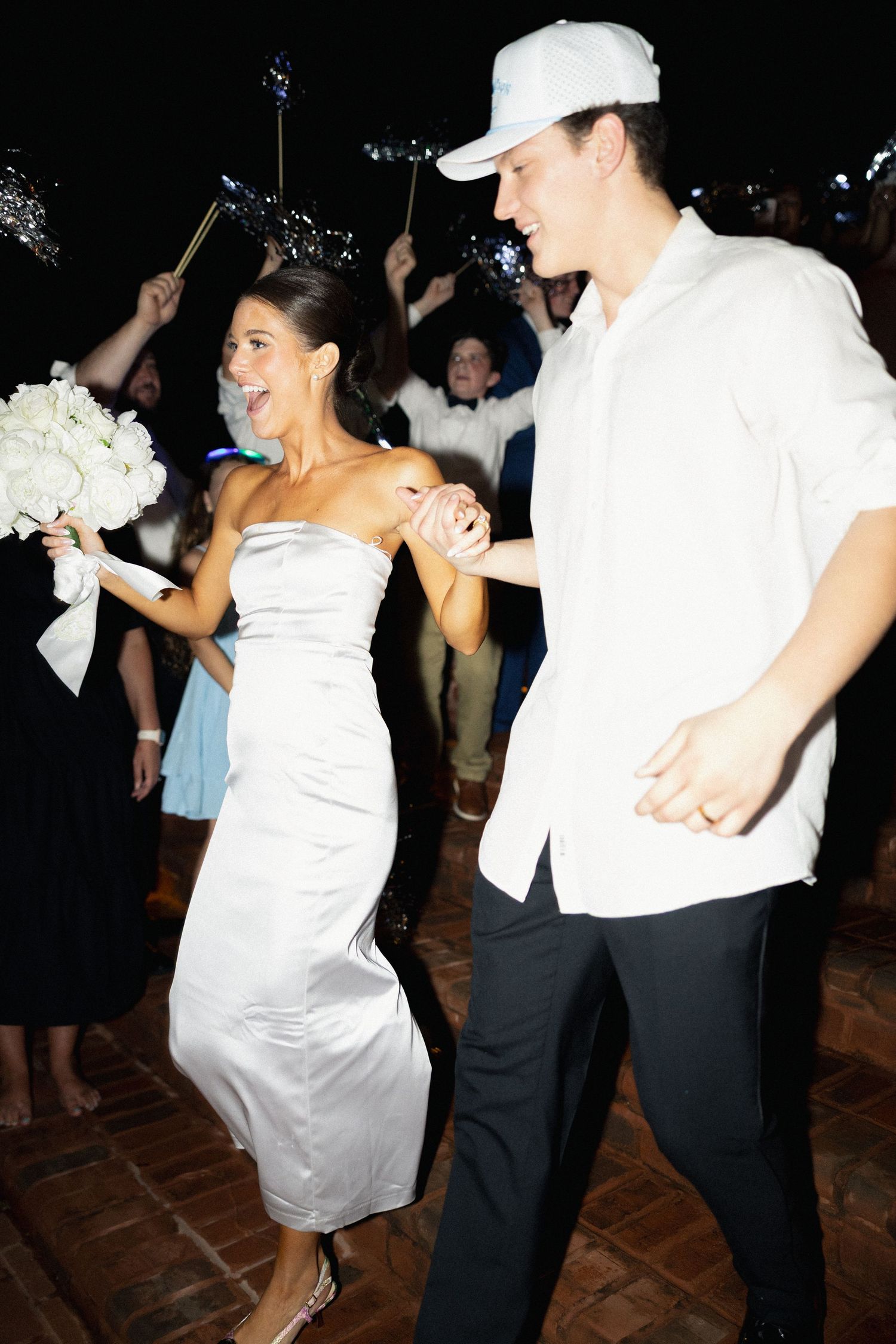 Newlyweds hold hands walking through sparkler send-off at night wedding reception.