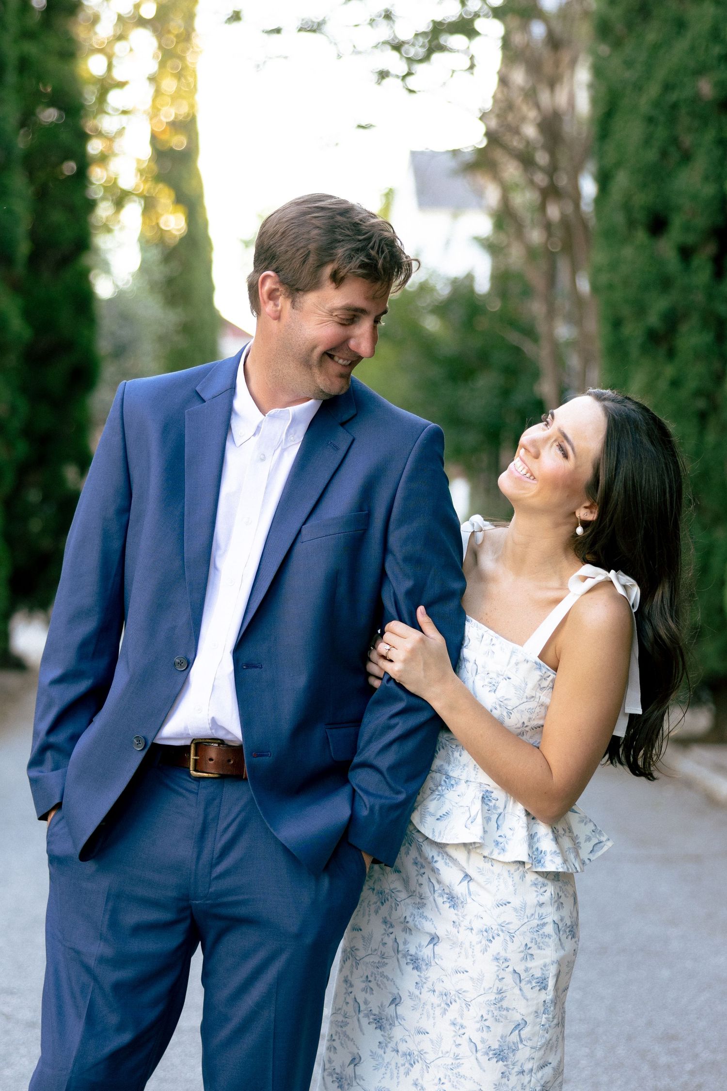Couple smiling at each other, man in blue suit, woman in floral dress, walking outdoors.