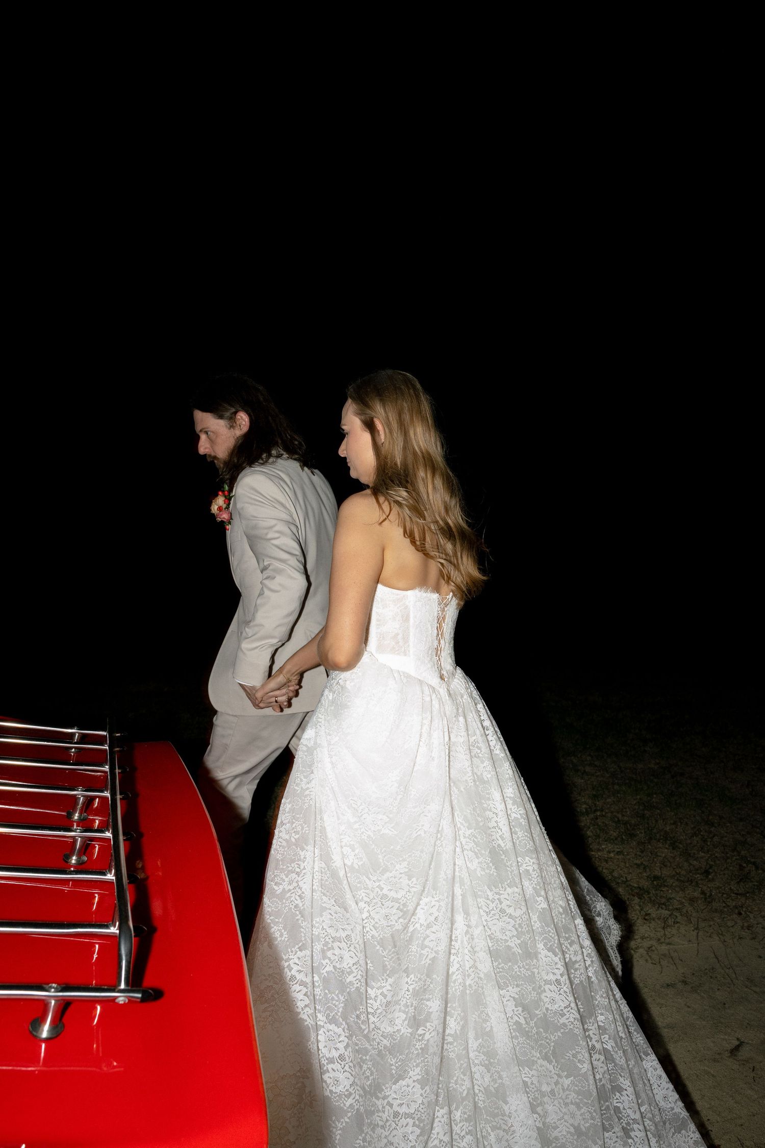 Bride and groom approaching red classic car for wedding getaway at night.