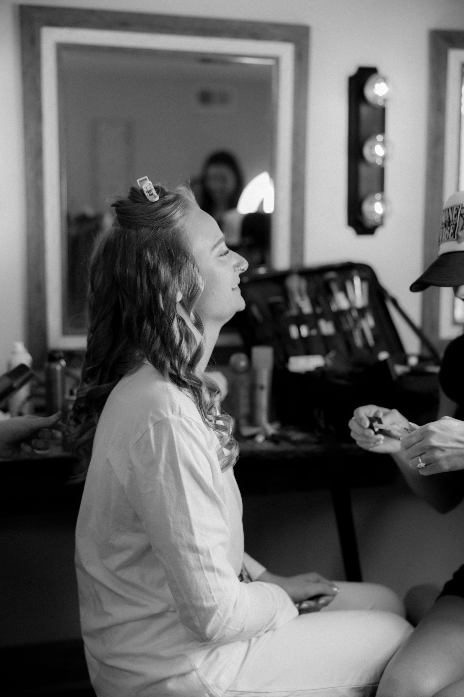 Black and white photo of bride laughing during hair and makeup preparations.