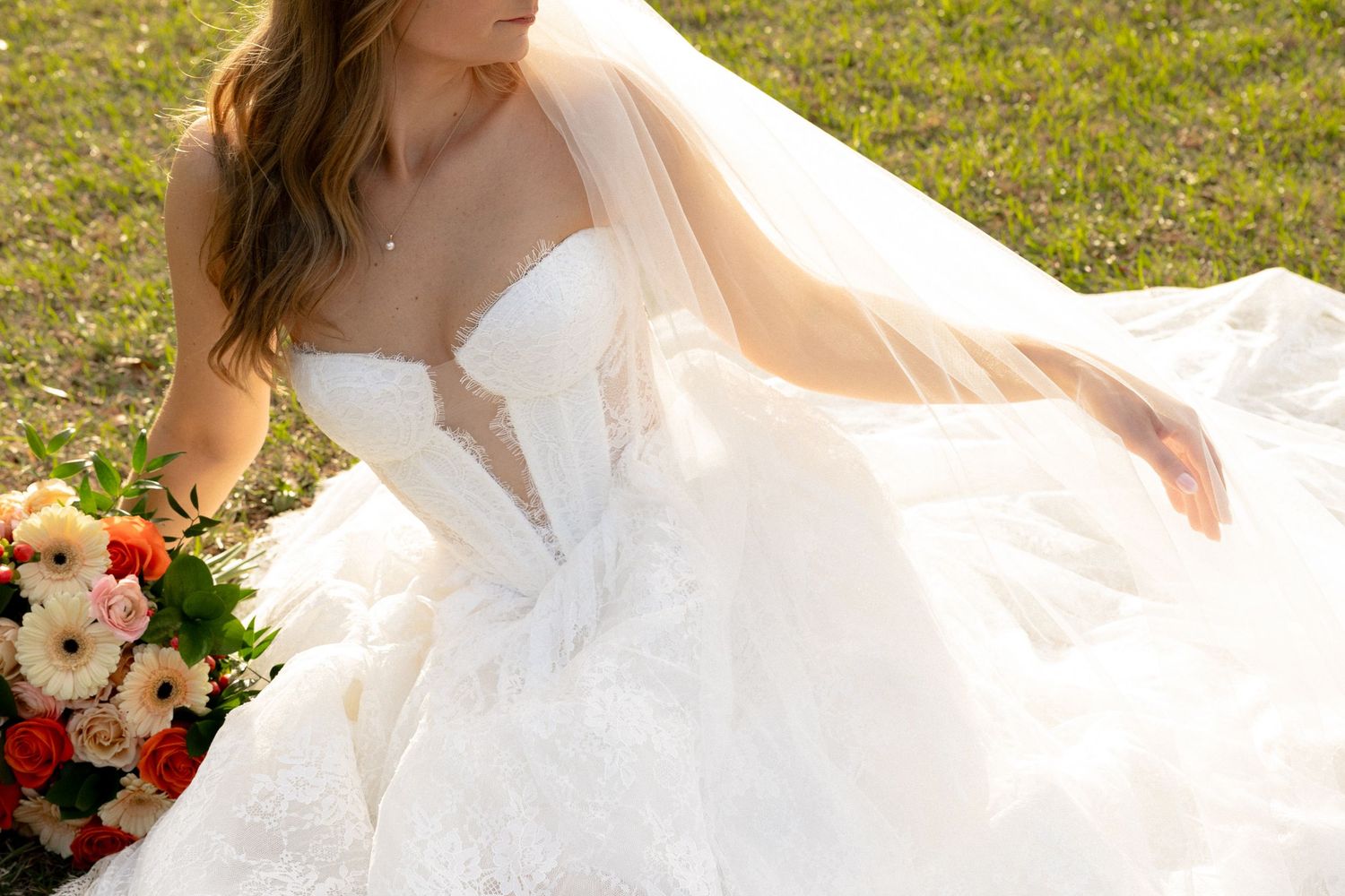 Close-up of bride in strapless lace wedding gown with colorful floral bouquet.