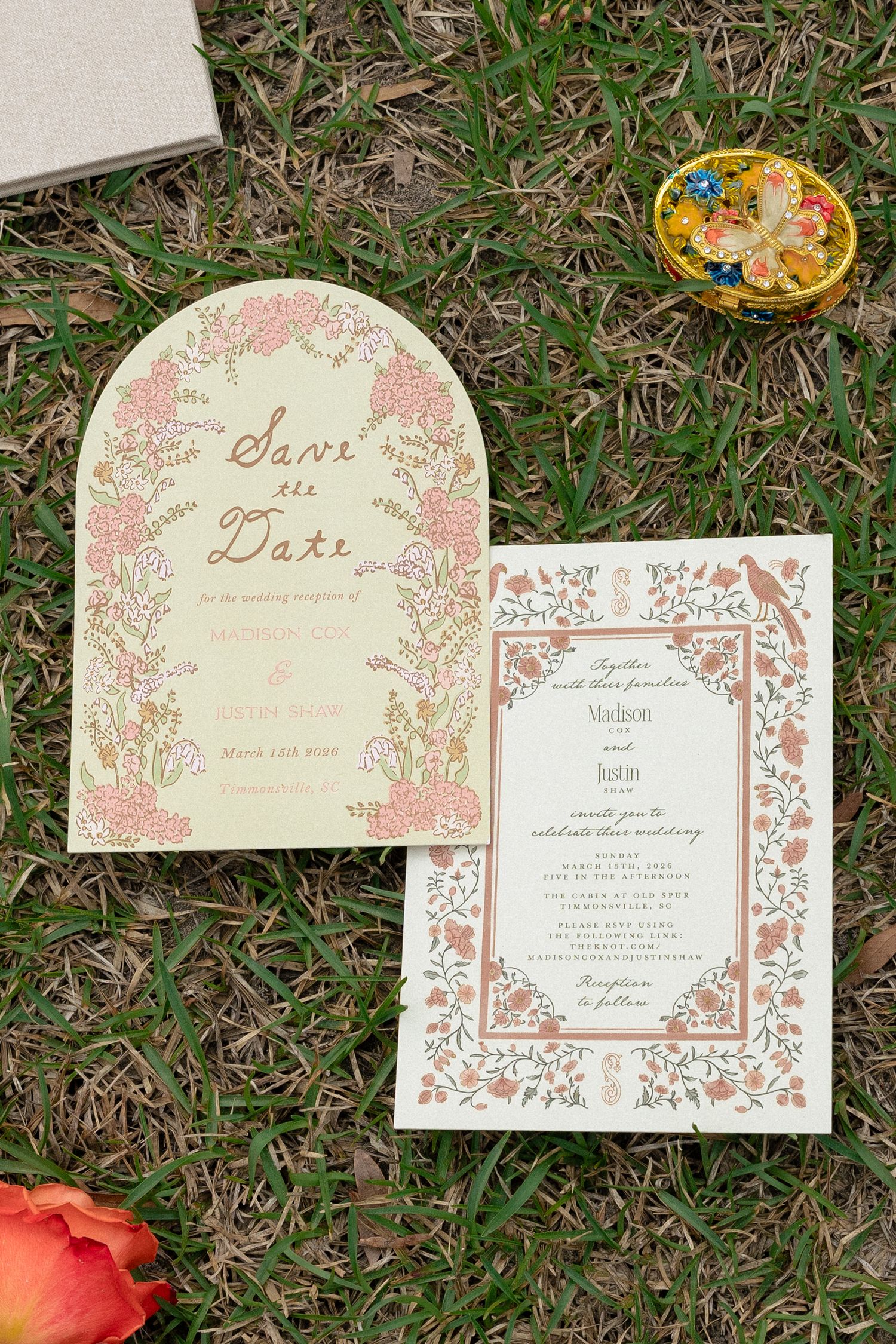 Floral arch-shaped Save the Date and botanical wedding invitation suite laid on green grass.