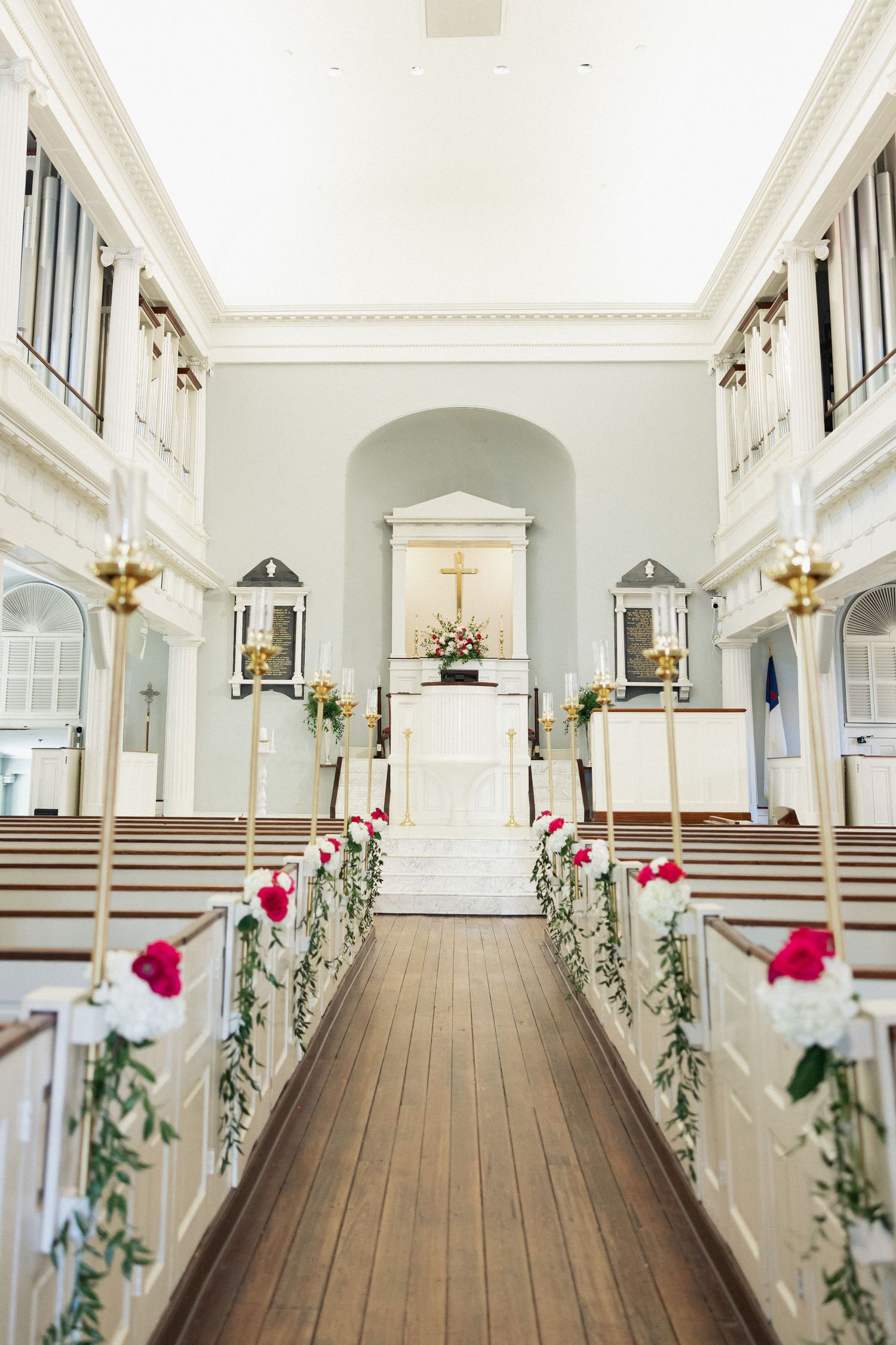 Elegant church wedding aisle decorated with pink roses and greenery leading to a white altar with a cross.