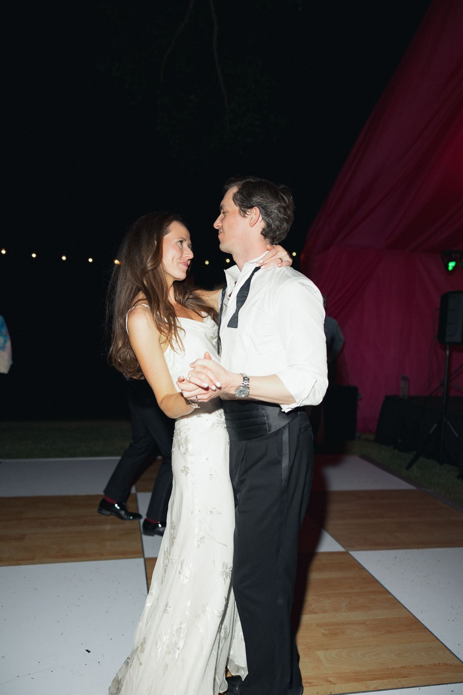 Bride and groom share romantic first dance on white dance floor at outdoor evening wedding reception.