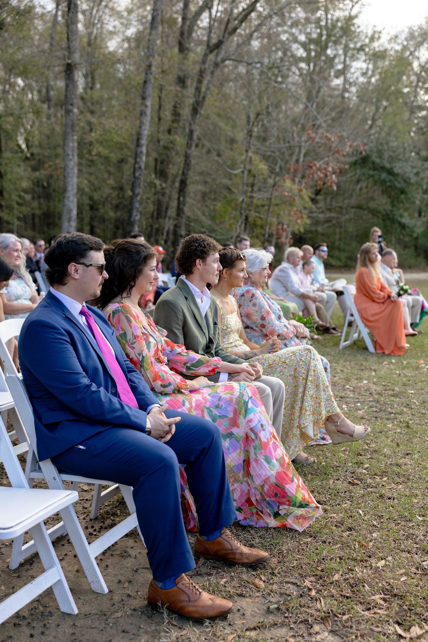 Wedding guests seated in white chairs watching outdoor ceremony surrounded by autumn trees.