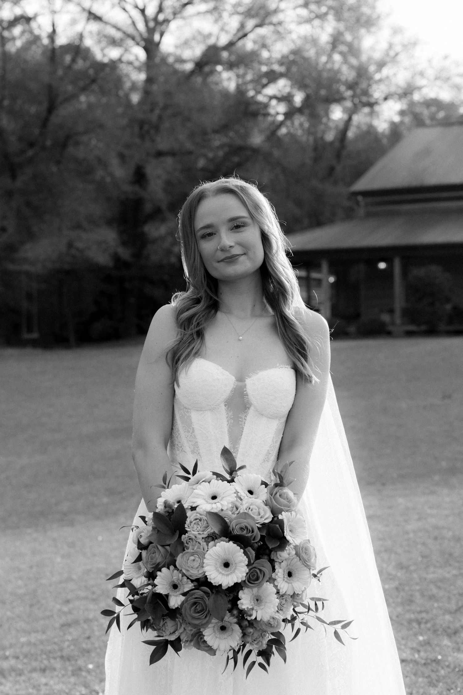 Black and white portrait of bride in strapless lace gown holding bouquet.