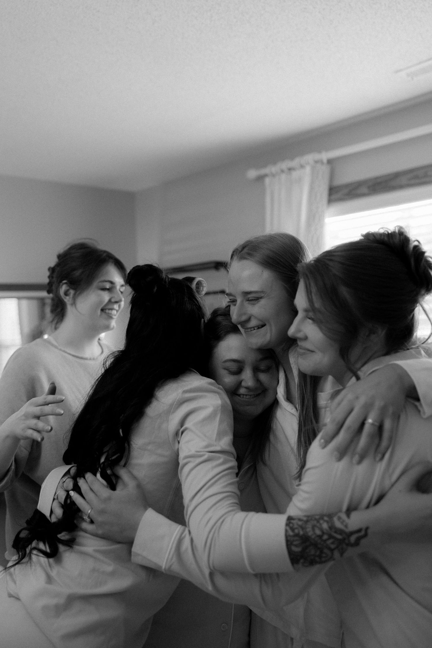 Black and white photo of bridesmaids sharing a warm group hug while getting ready together.