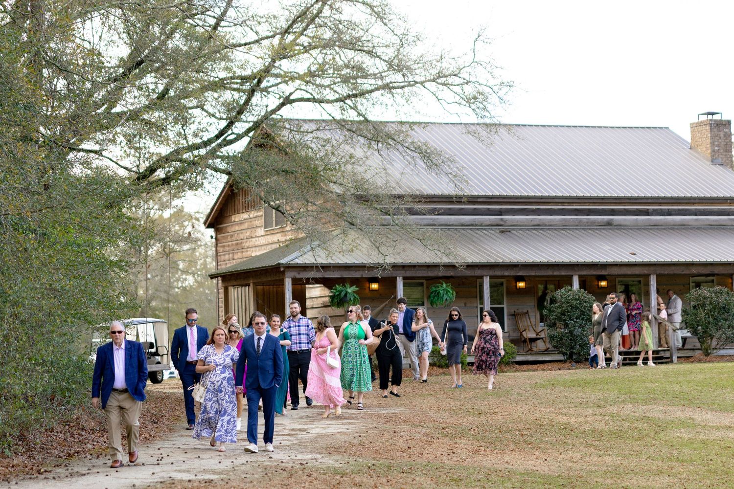 Wedding guests walking toward a rustic barn venue surrounded by trees at an outdoor wedding celebration.