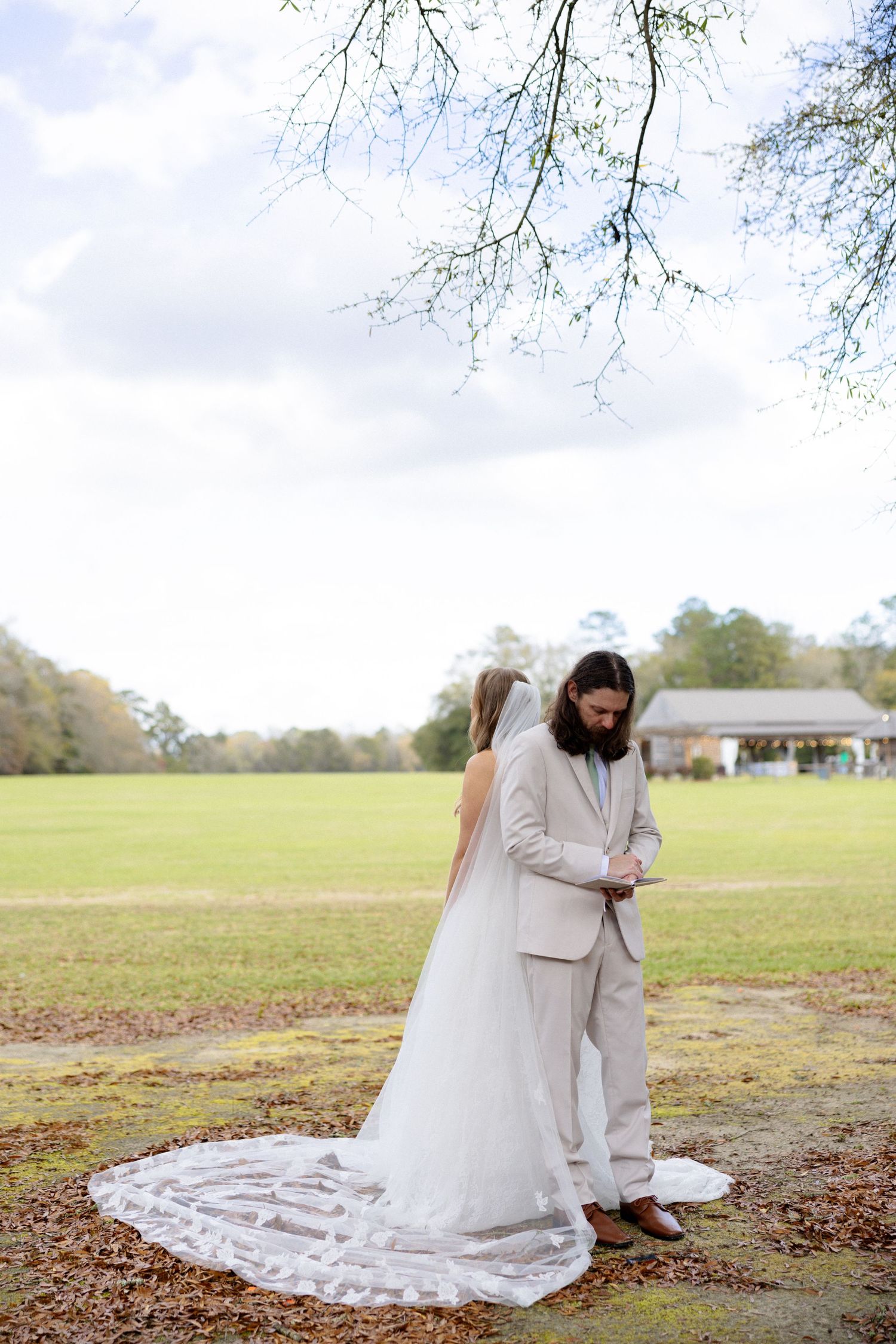 Bride and groom share intimate moment in open field, bride wearing cathedral veil and lace gown.