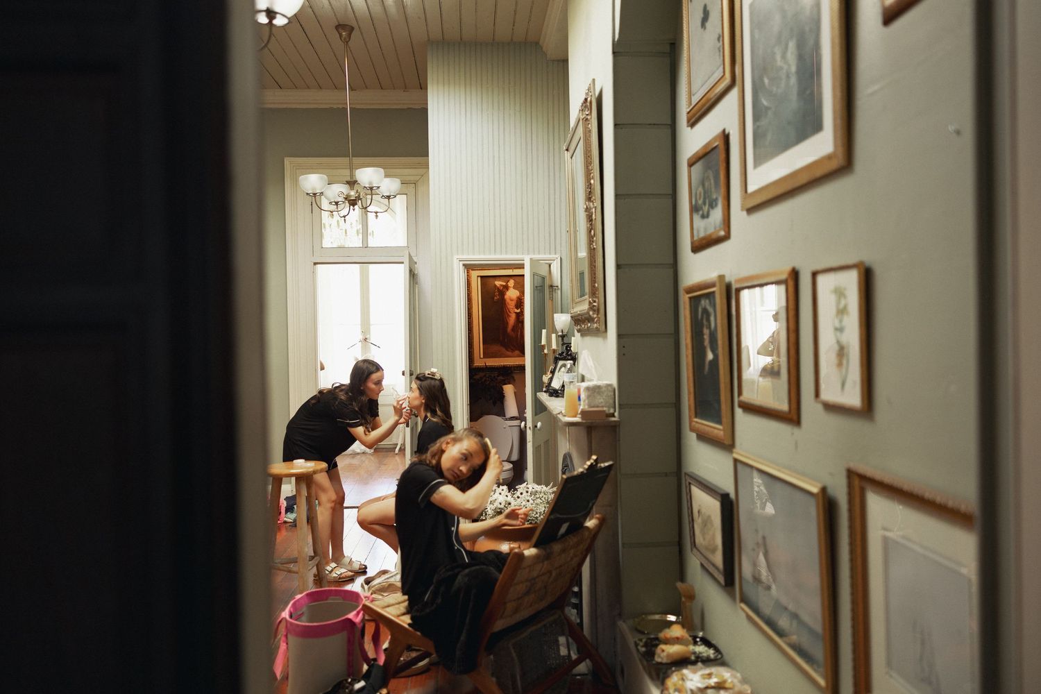 People gathered in a hallway adorned with framed photos, engaged in hair and makeup preparation.