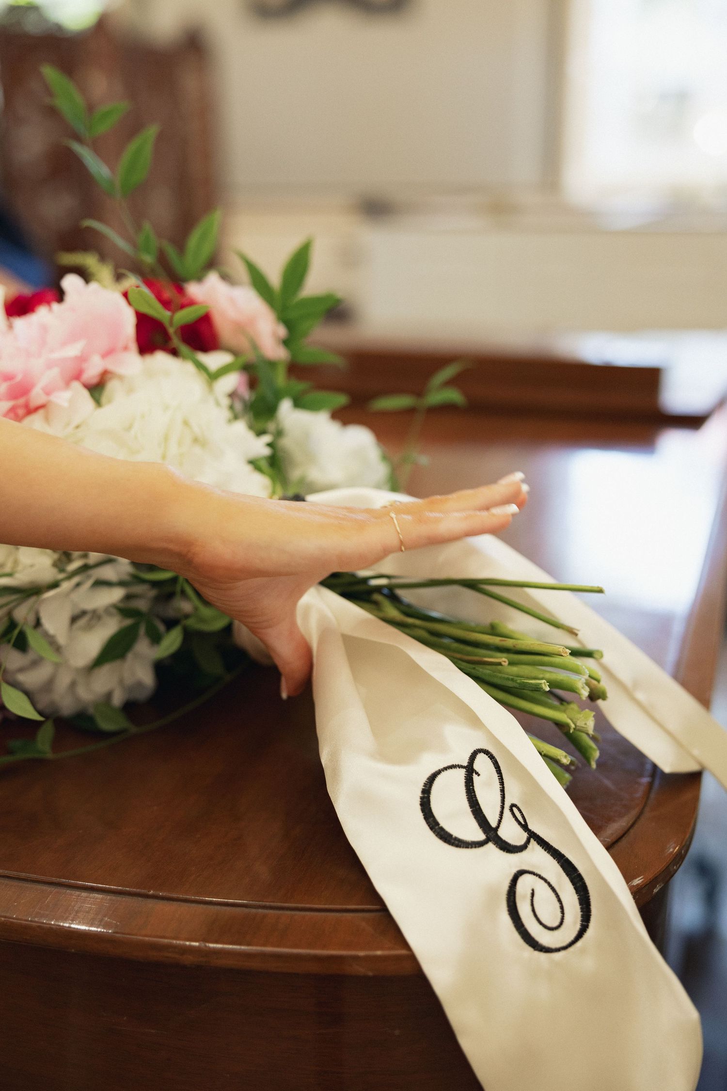 Bridal bouquet of pink peonies and white hydrangeas with monogram ribbon on wooden table.