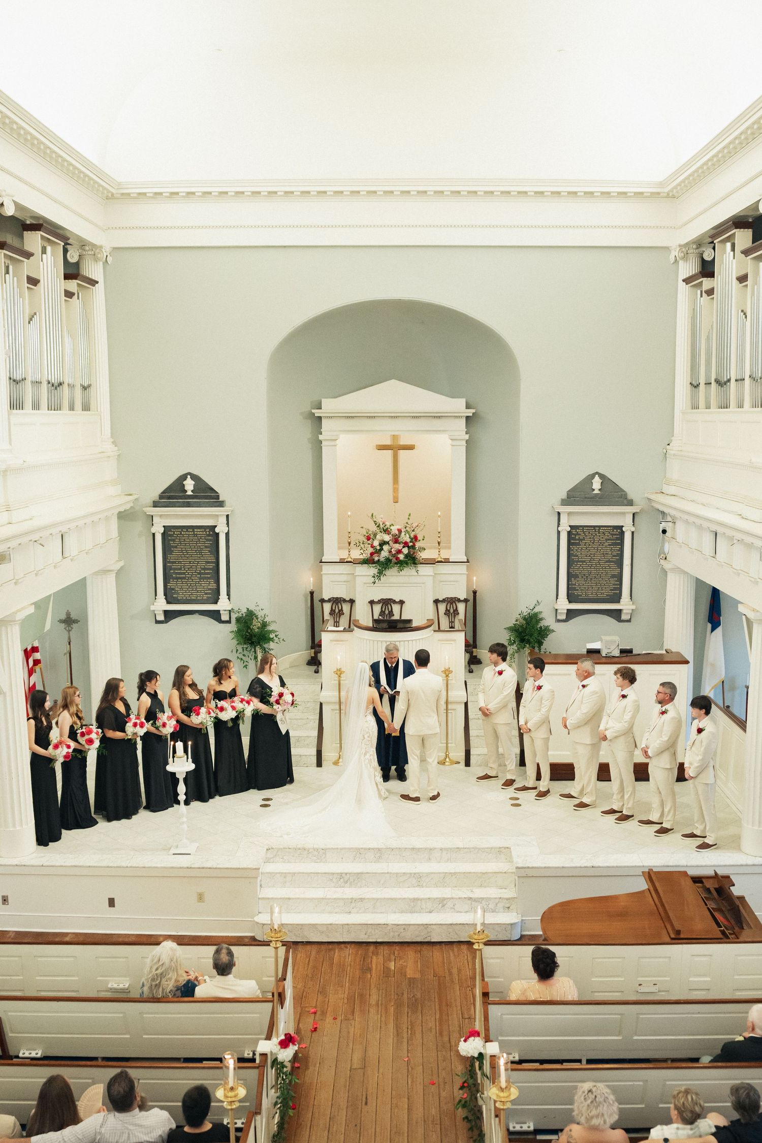Overhead view of wedding ceremony with bridesmaids in black and groomsmen in cream suits at the altar.