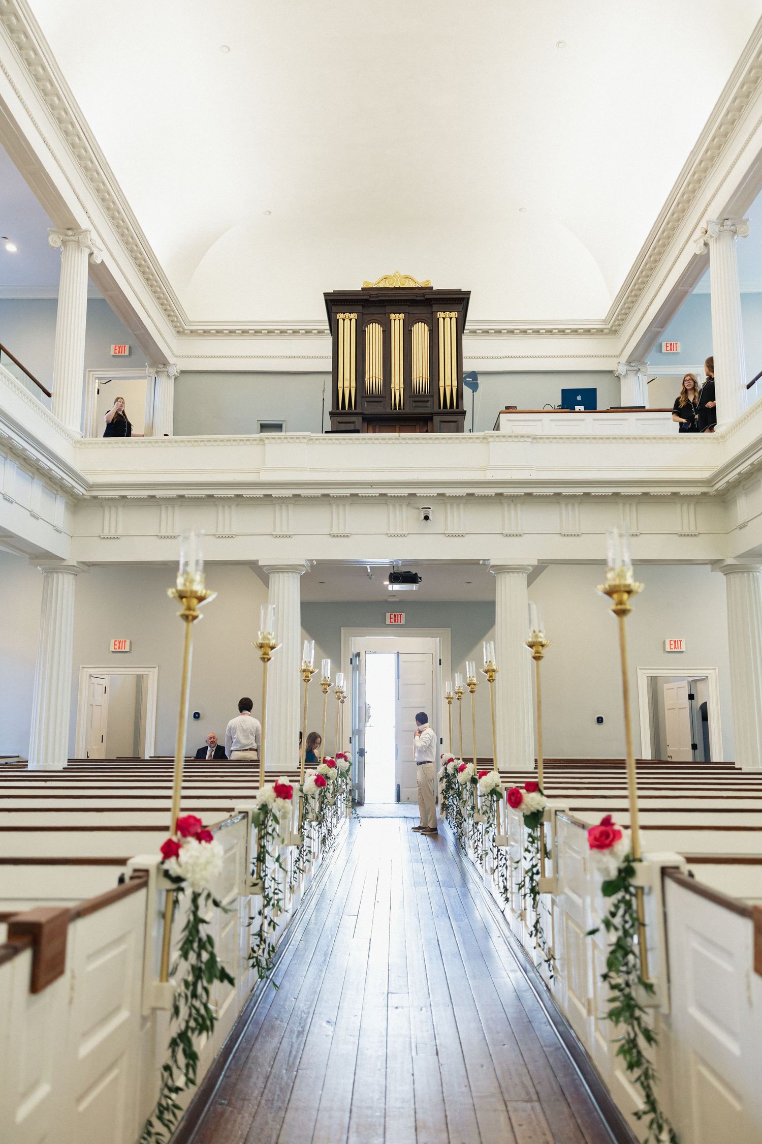 Classic church wedding aisle decorated with red roses and greenery, featuring a pipe organ loft.