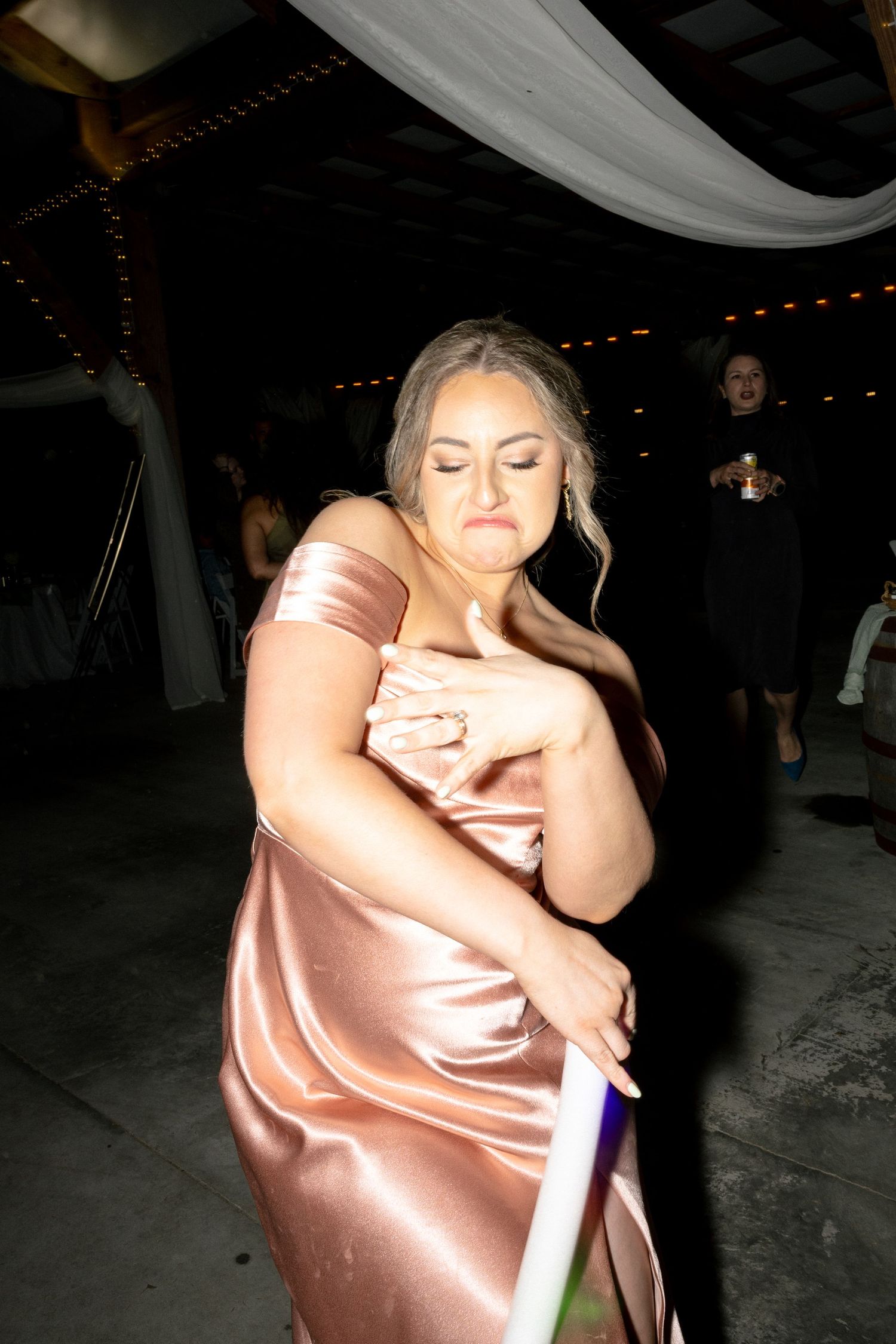 Woman in pink satin gown dances with eyes closed holding a light-up stick at wedding reception.