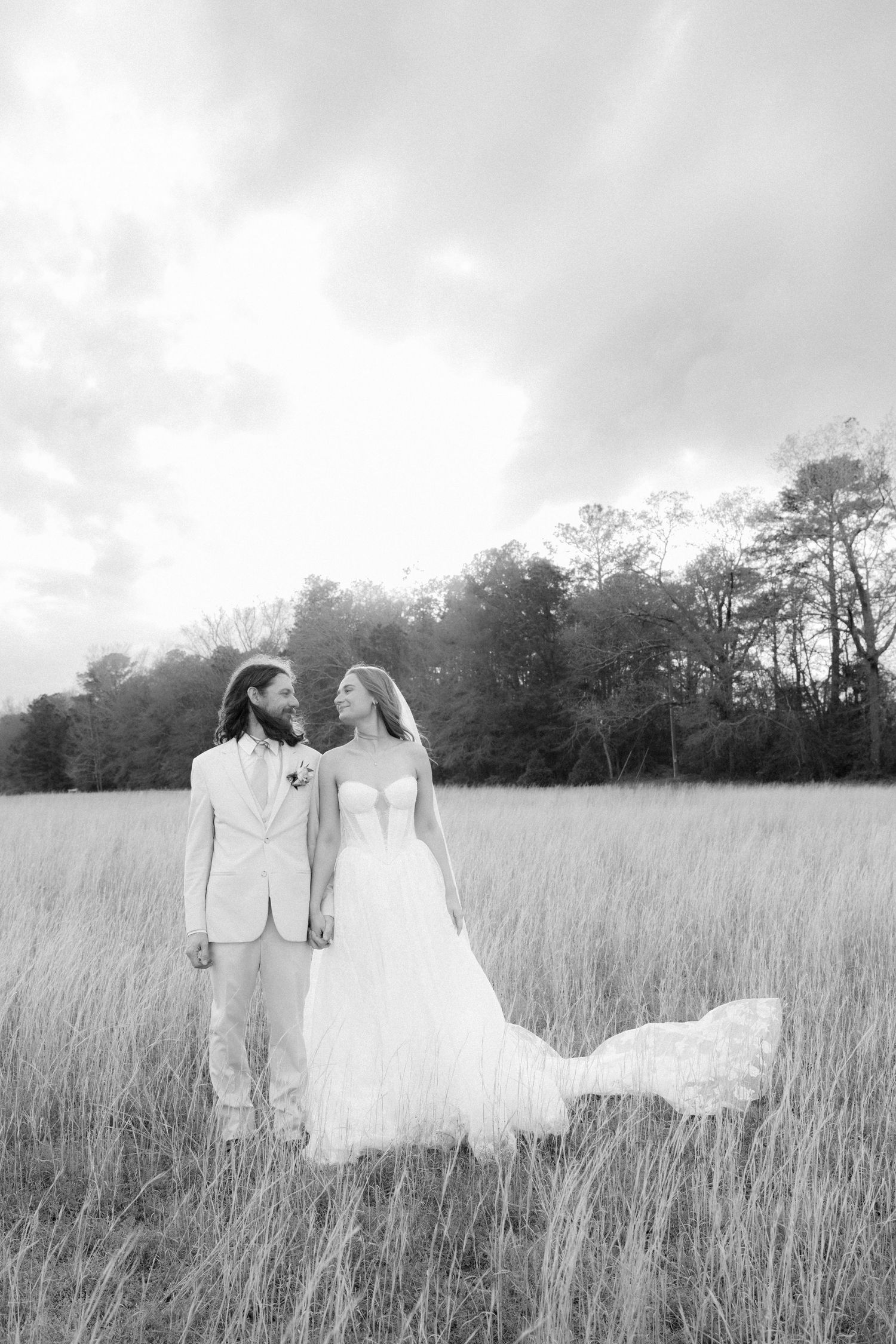 Black and white photo of bride and groom holding hands in a sweeping golden grass field.