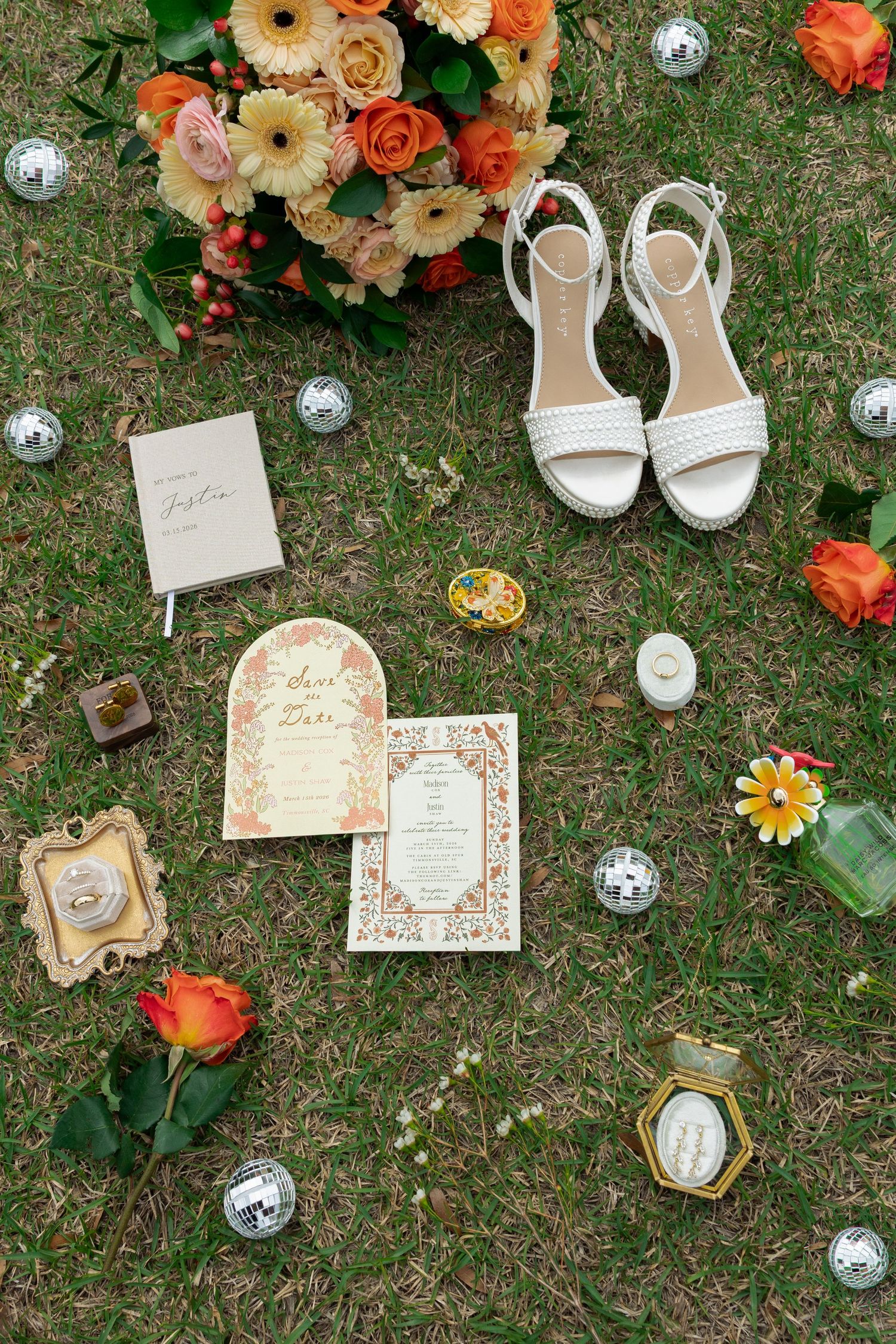 Flat lay of wedding details including floral bouquet, shoes, invitations, and rings on green grass.