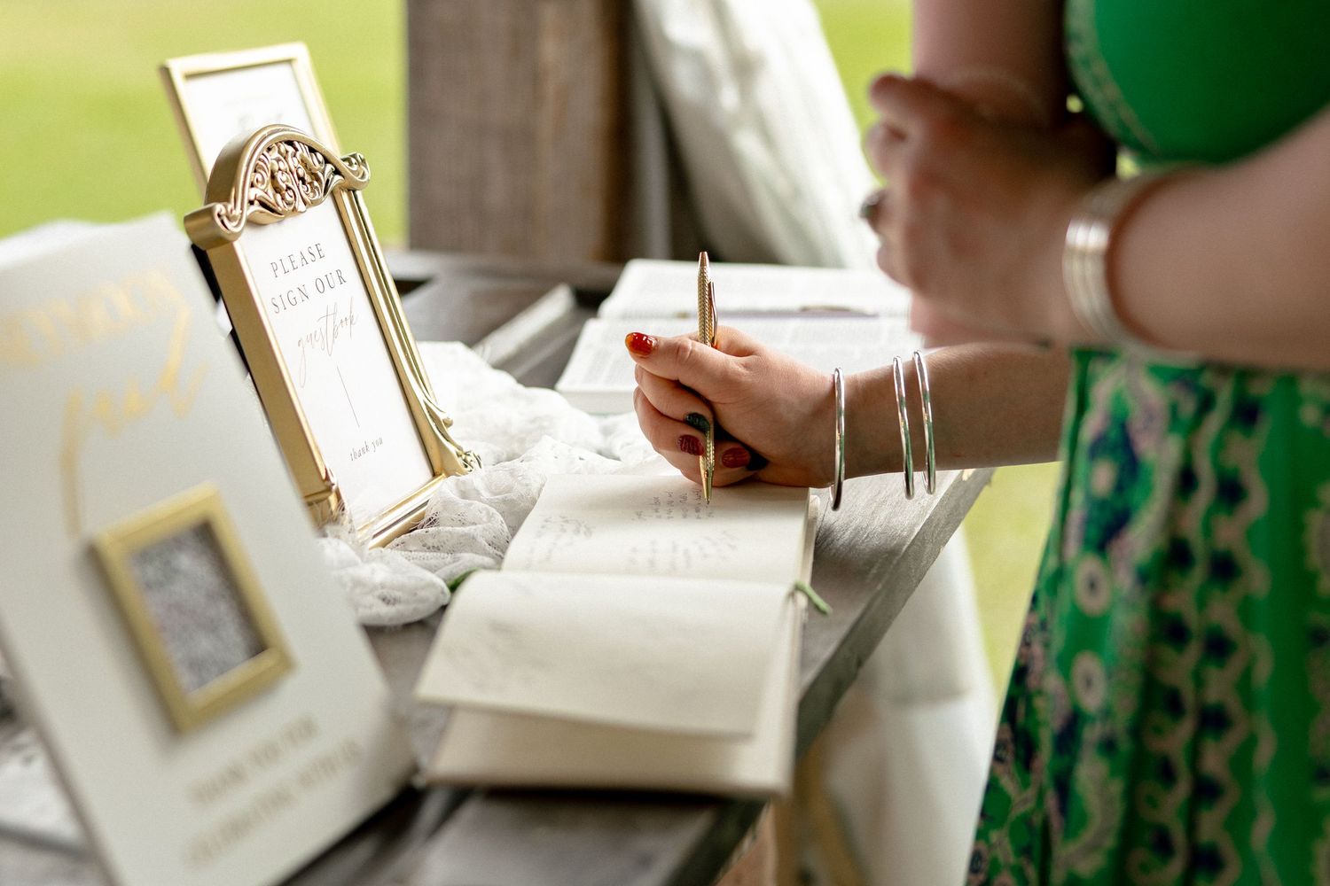 Close-up of wedding guest signing guestbook with gold pen at decorated barrel table.