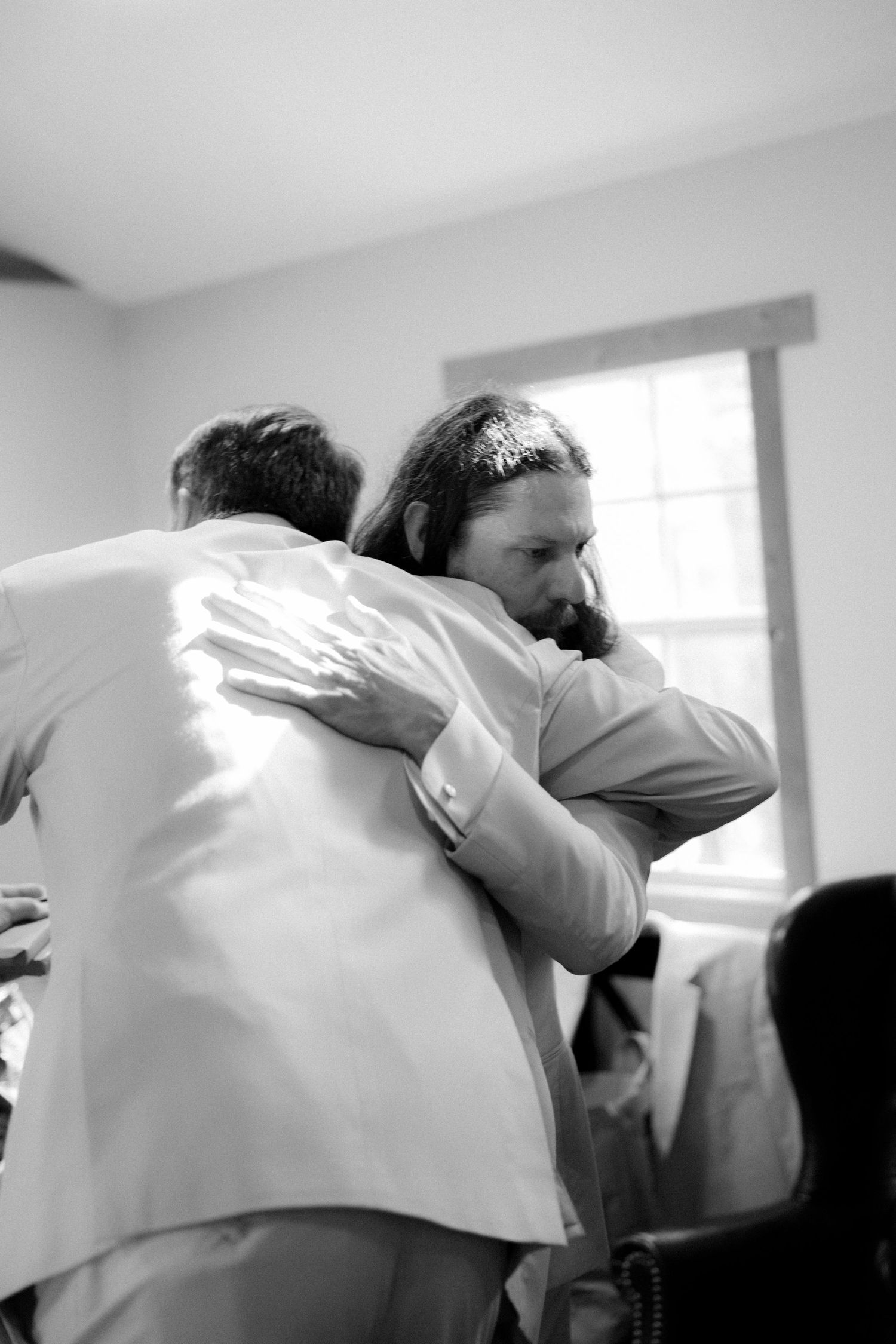 Black and white photo of two groomsmen sharing an emotional embrace before a wedding ceremony.