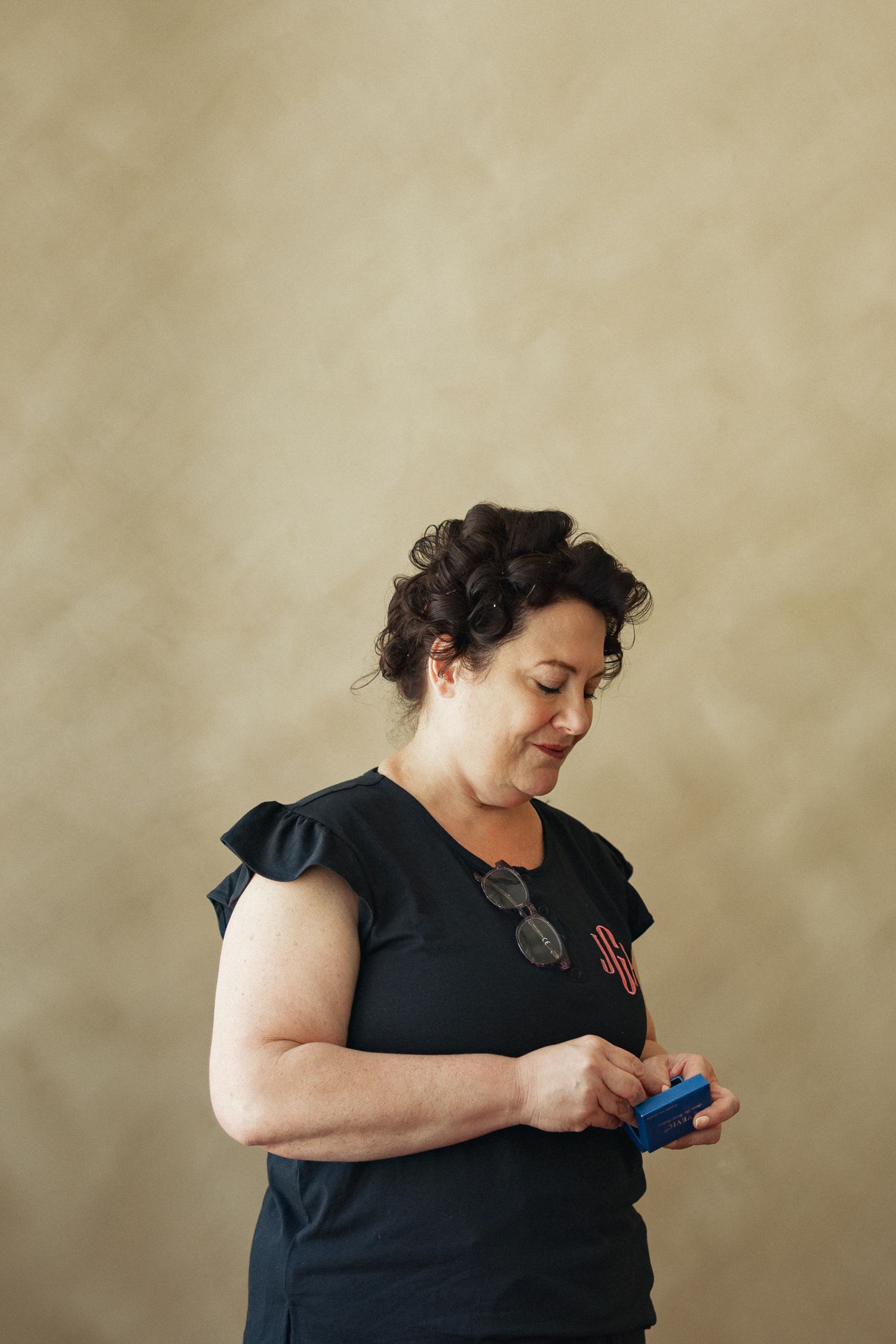 A woman in a black top looks down at a blue object she holds in her hands.