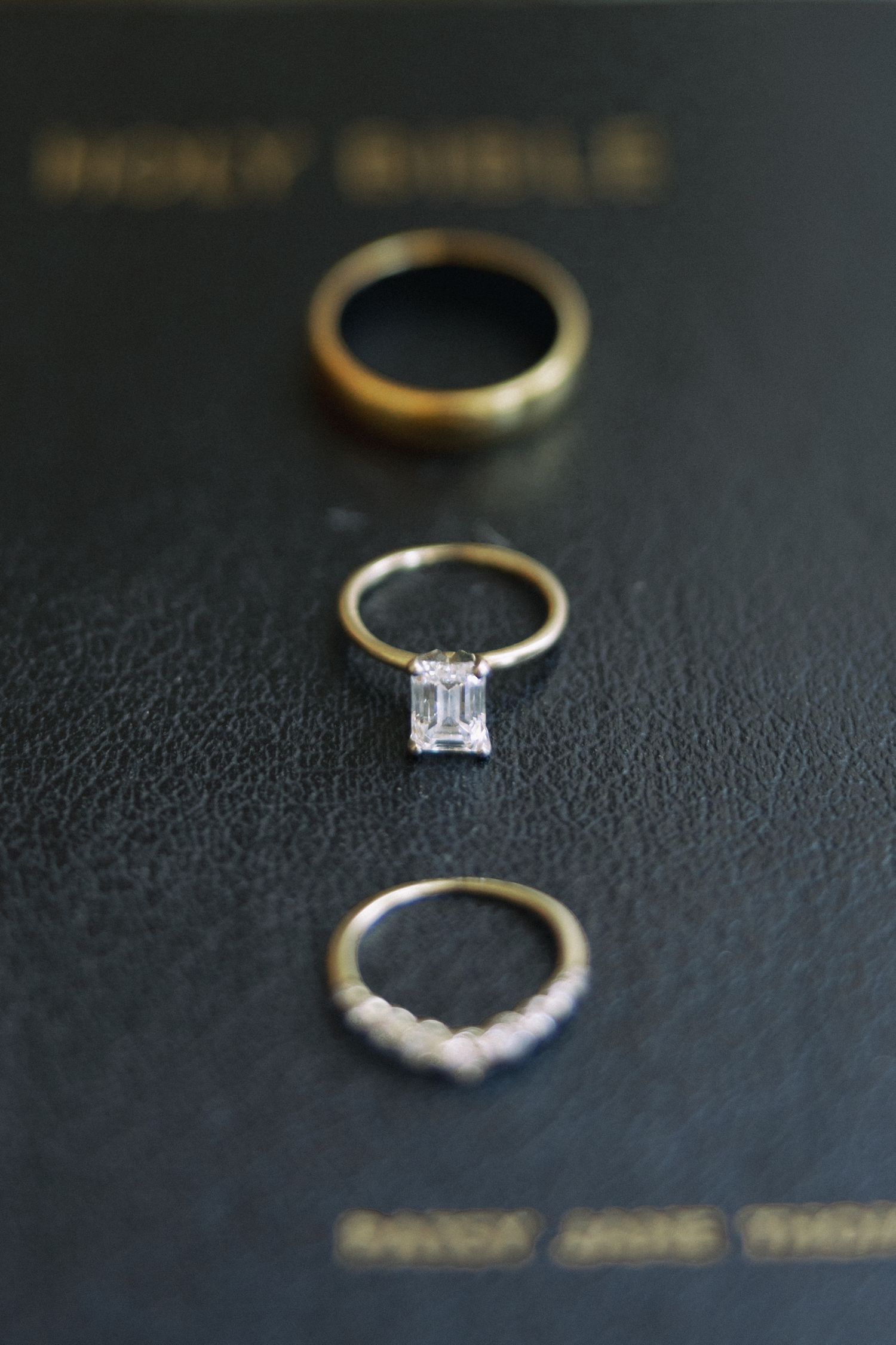 Three gold wedding rings including a solitaire emerald cut diamond engagement ring displayed on a Holy Bible.