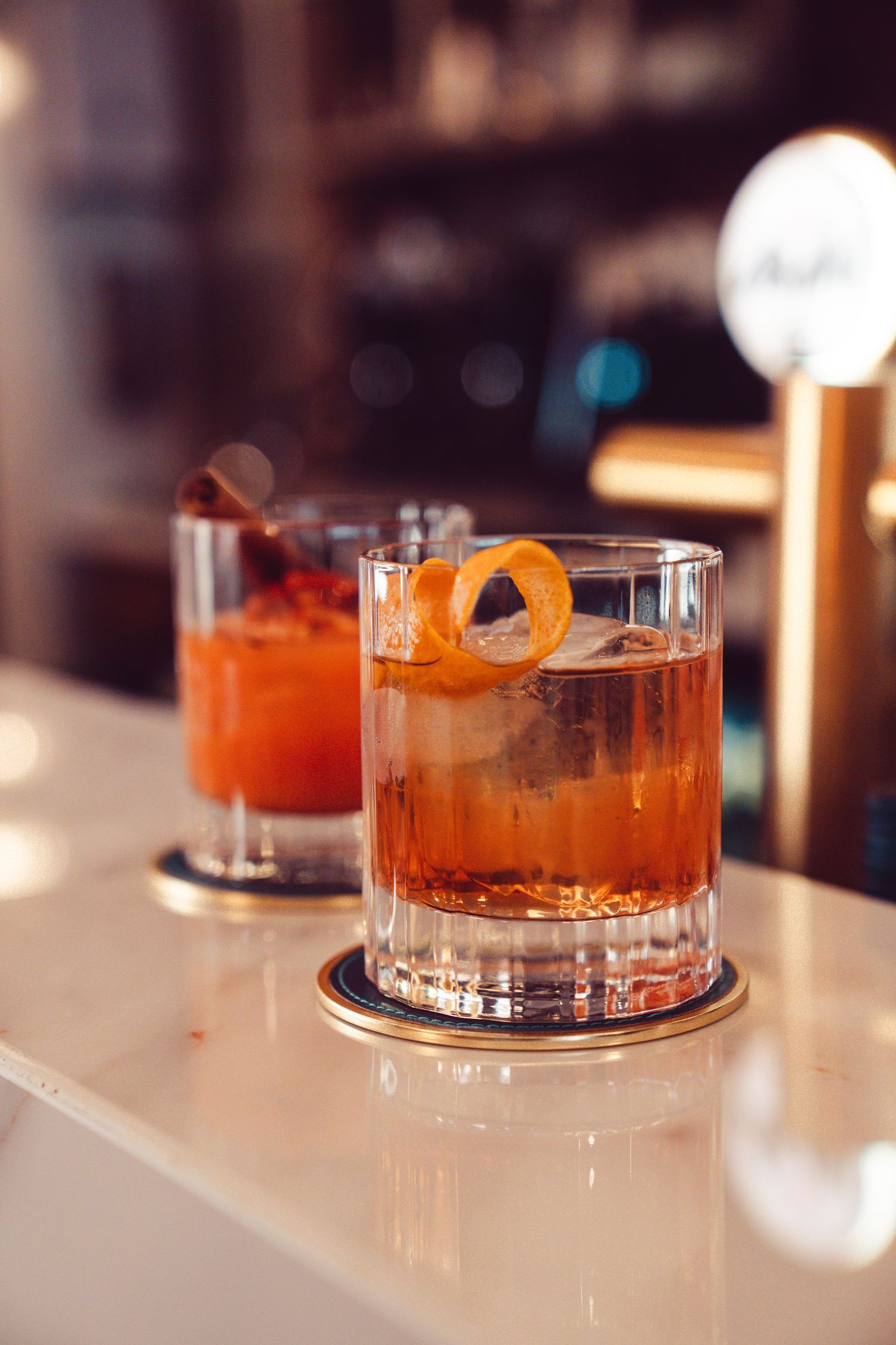 Elegant craft cocktails garnished with orange peels served in crystal glasses on a white bar counter.