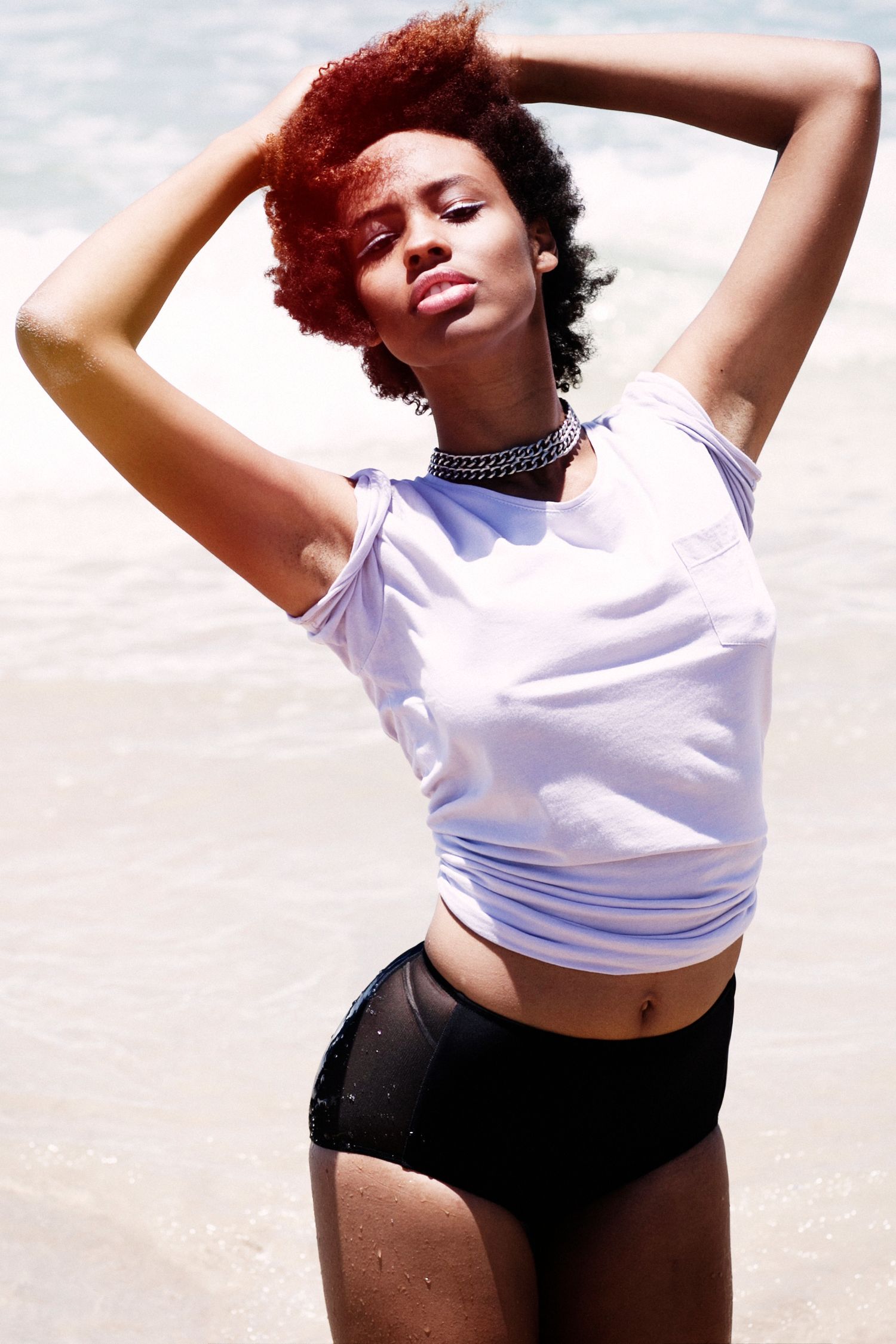 Model in white crop top and black shorts poses expressively against bright background.