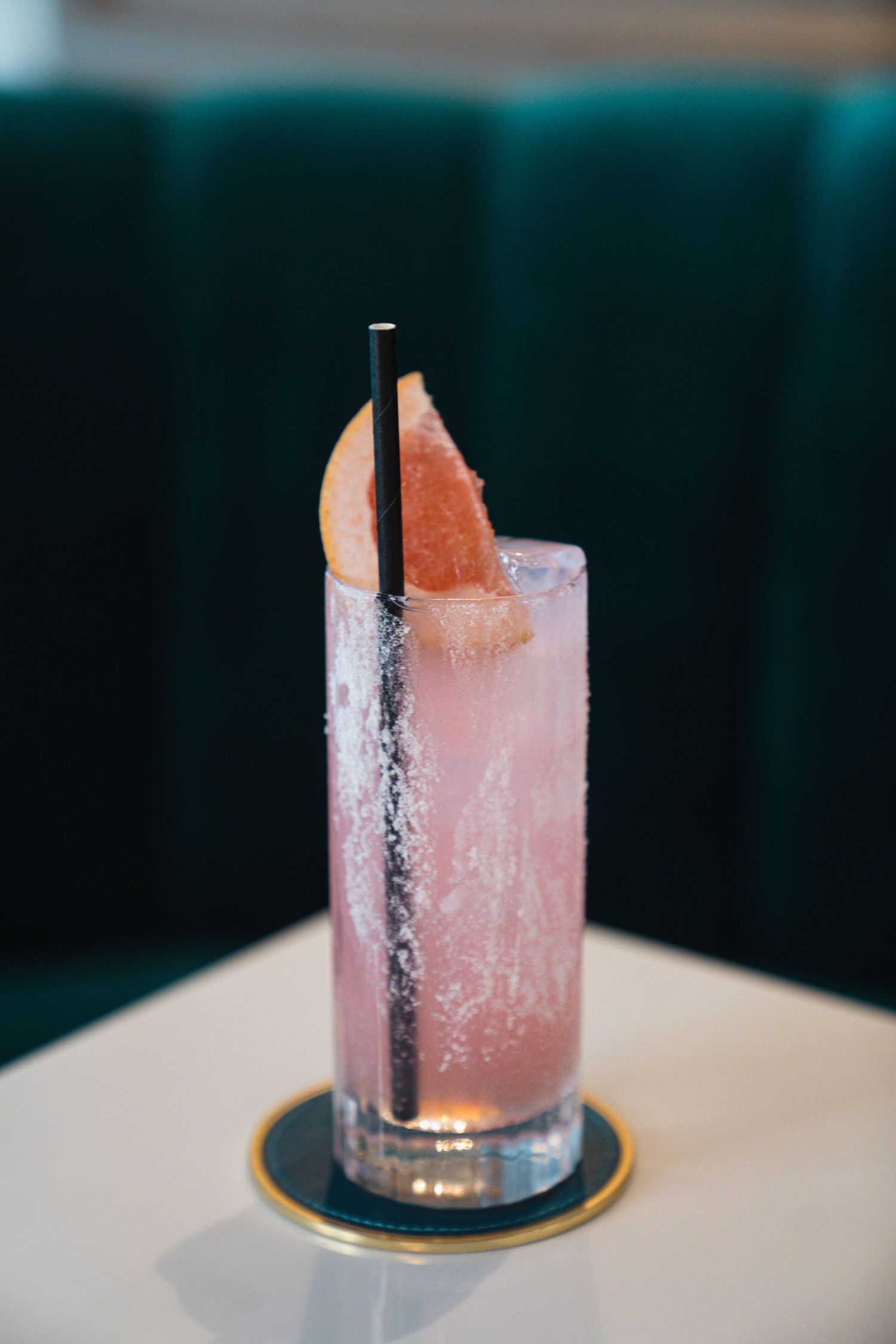 Pink-hued craft cocktail served in a glass with a frosted ice block garnish against a teal backdrop.