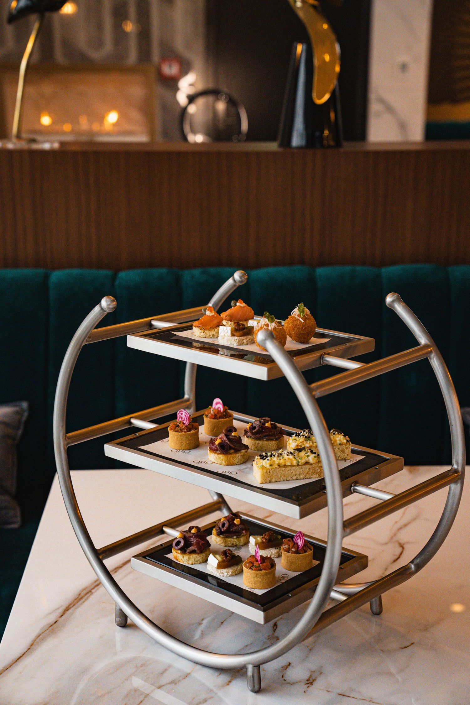 Elegant three-tiered dessert stand displaying colorful petit fours and pastries on a marble table in a restaurant setting.