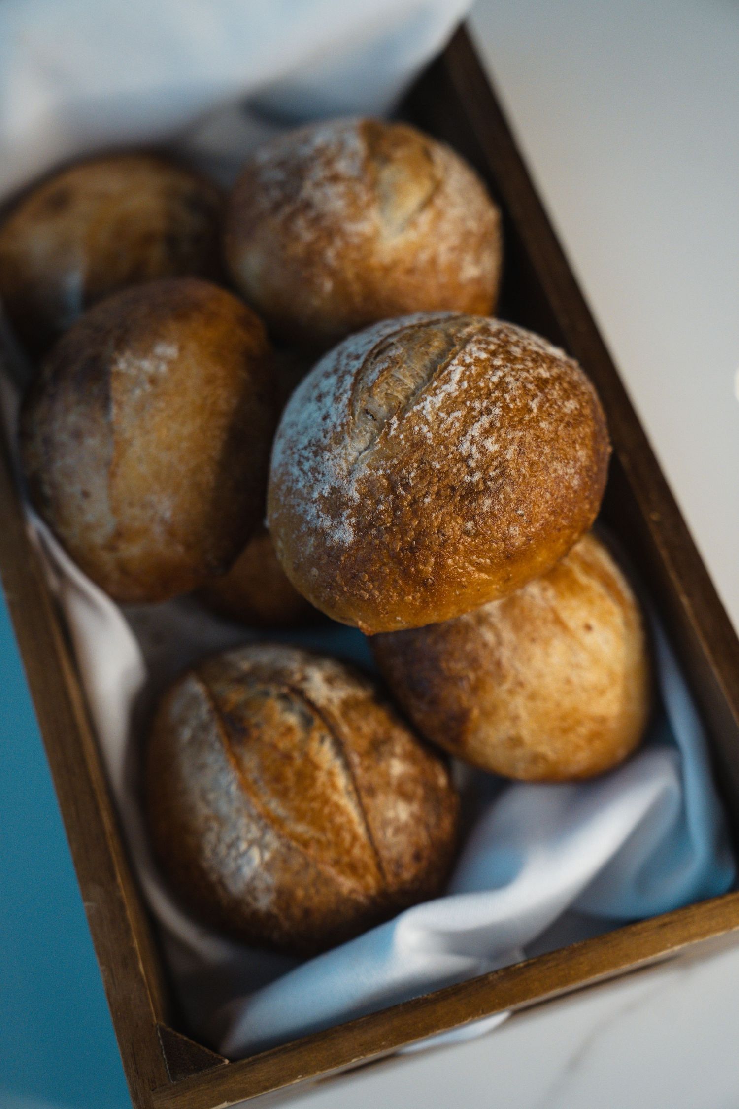 Freshly baked rustic dinner rolls served in a dark wooden box with a white napkin.