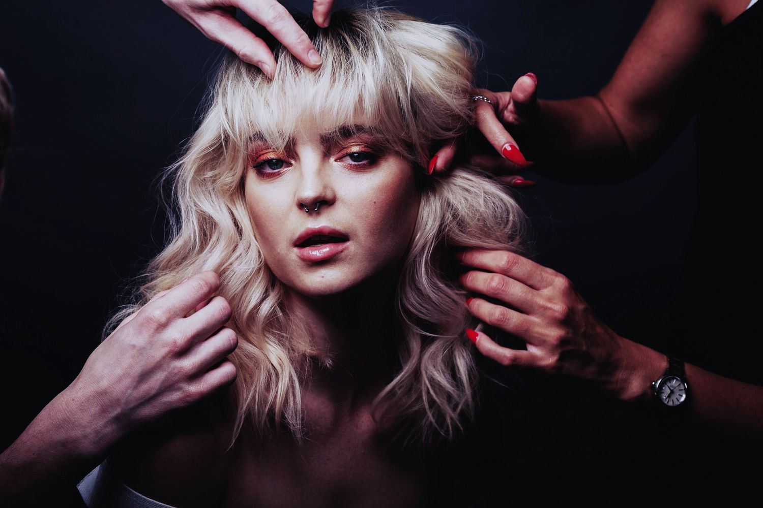 Multiple shots of a blonde model with bangs posing against dark background while hands style and frame their face.