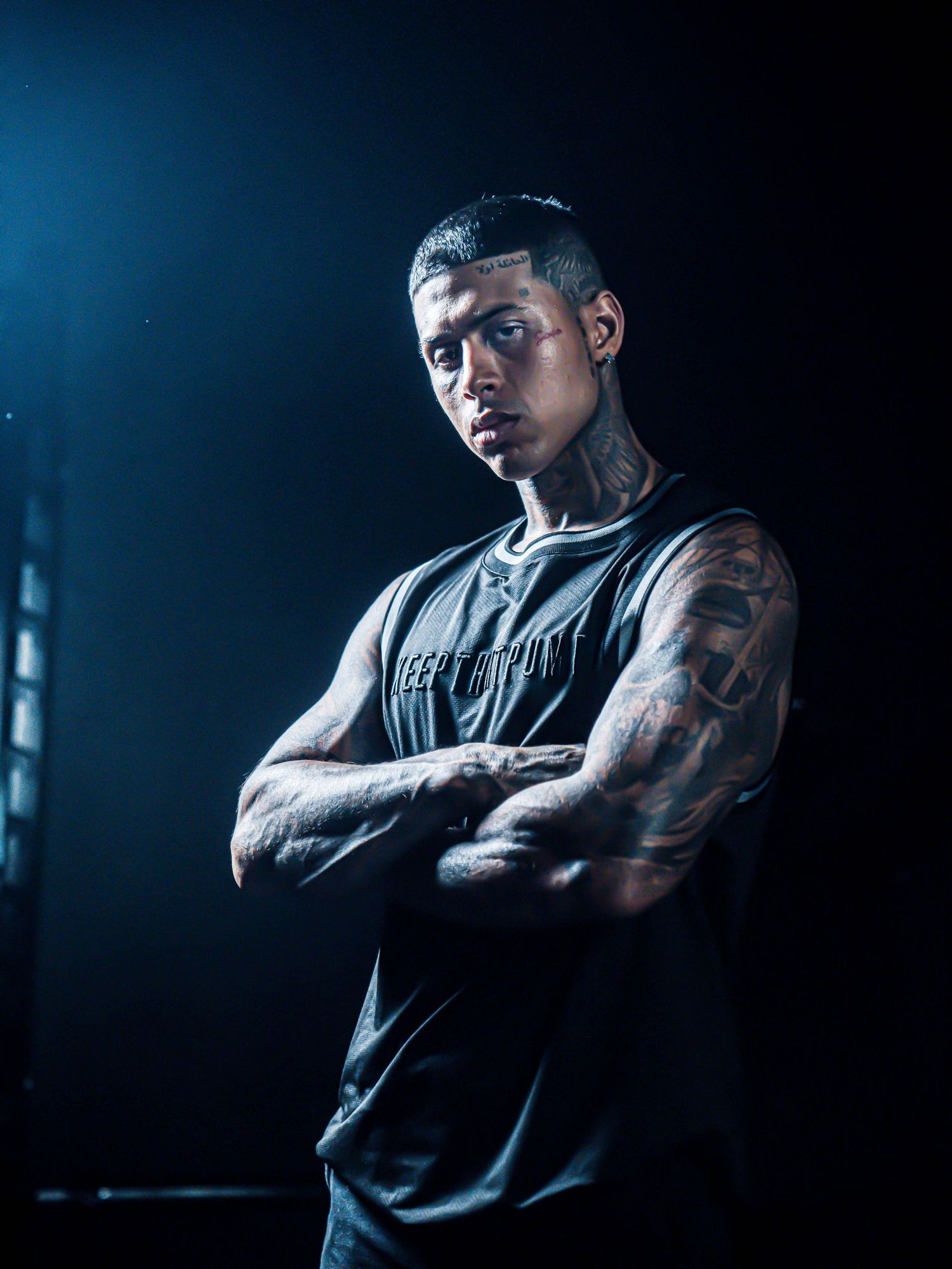 Dramatic portraits of muscular person in sleeveless shirt against blue-toned background.